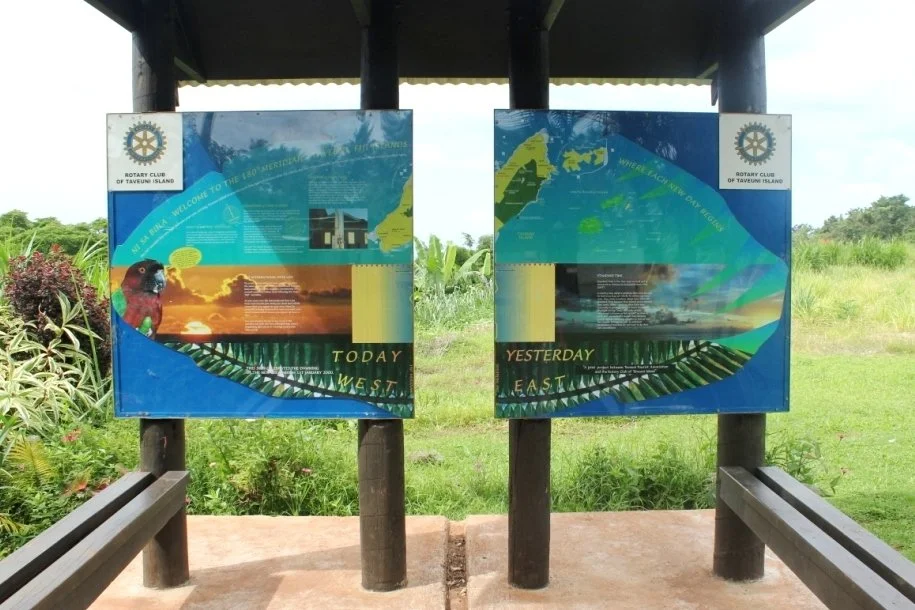 Information boards about Taveuni Island, featuring a map, a koala, and sunset images, with a backdrop of lush green vegetation.