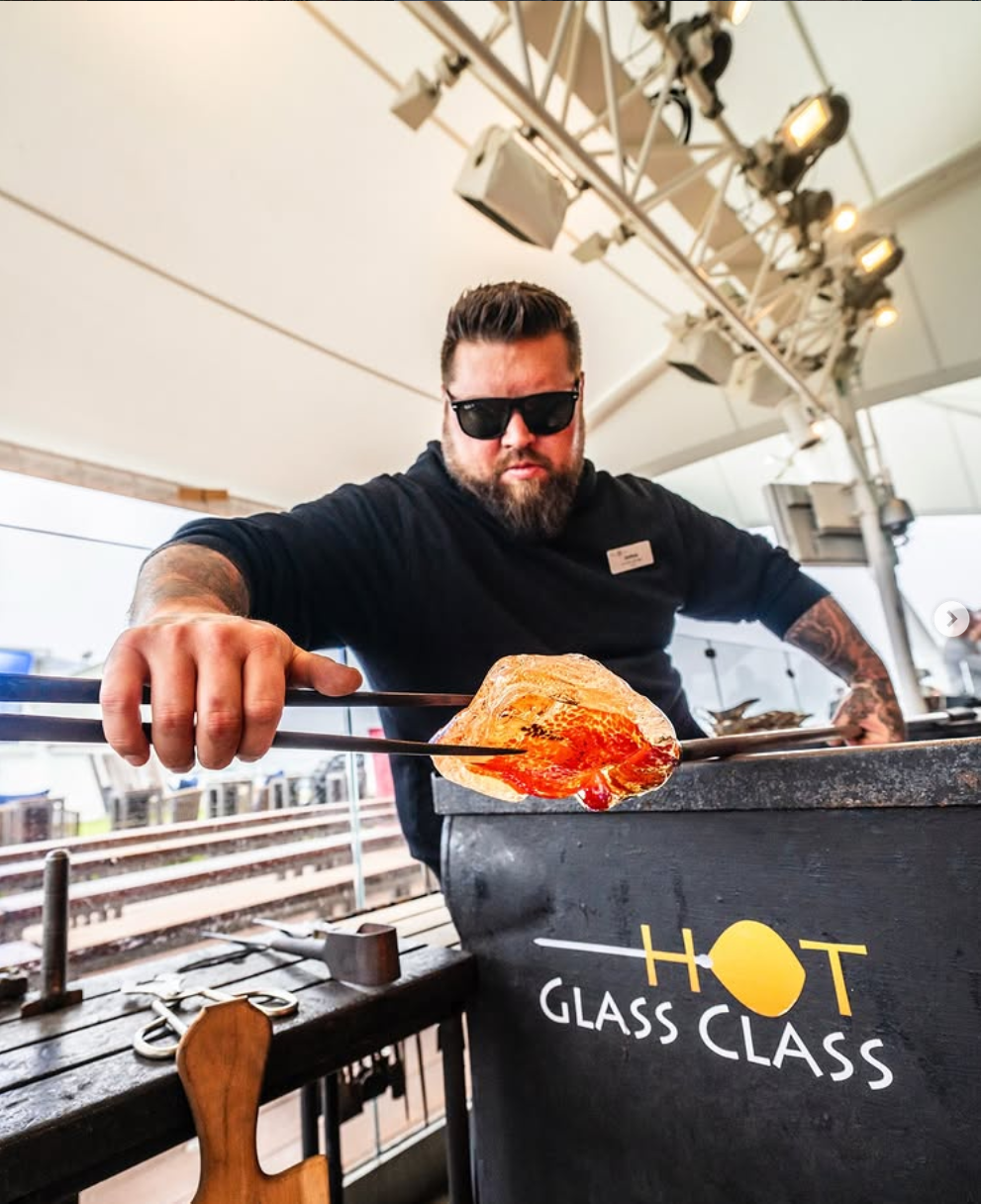 Man with sunglasses is cooking a tortilla or flatbread on a grill, using tongs inside a tent at a food event.