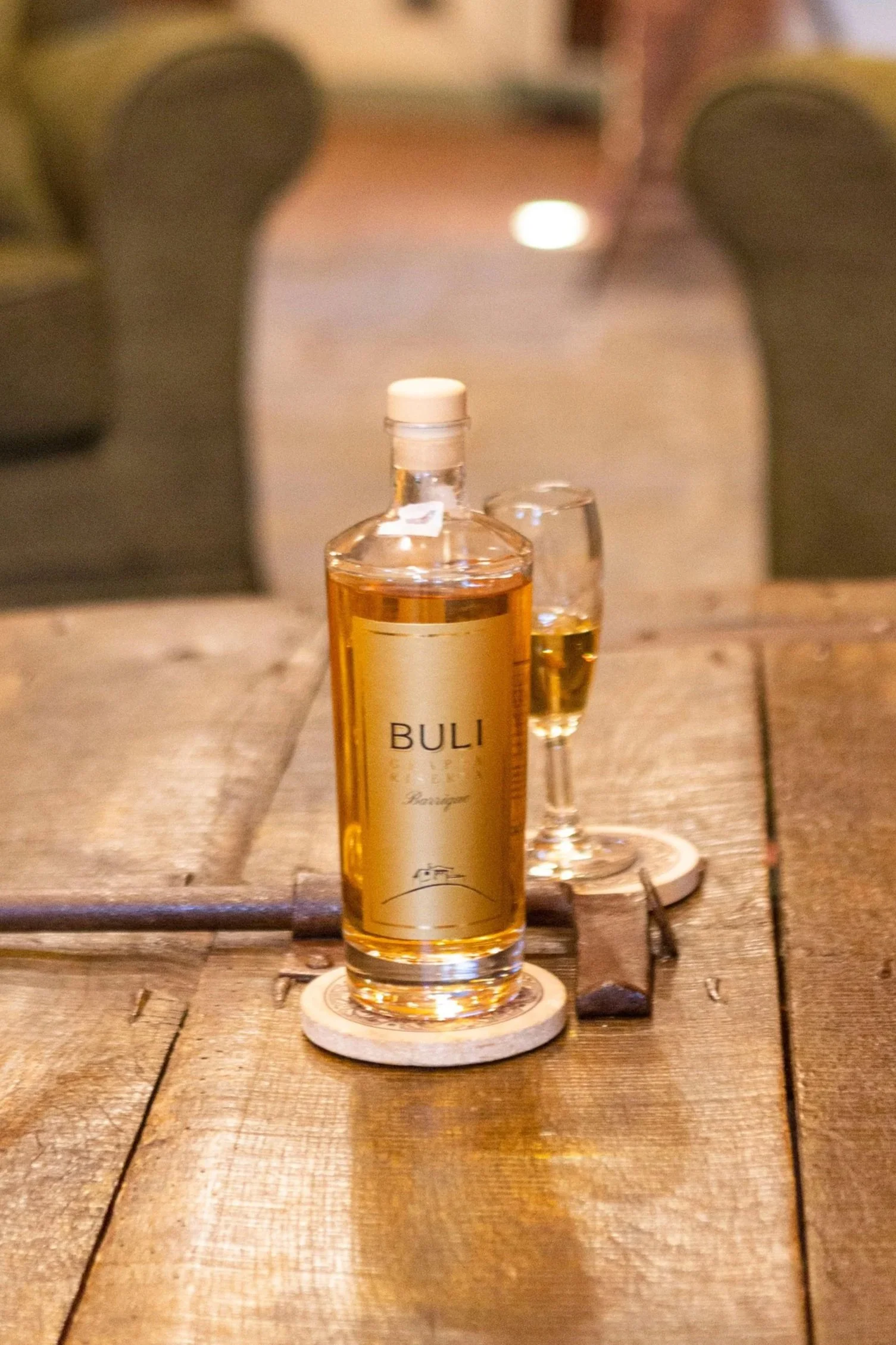A bottle of BULLI beverage and a glass filled with the same beverage on a wooden table, with a blurry background.