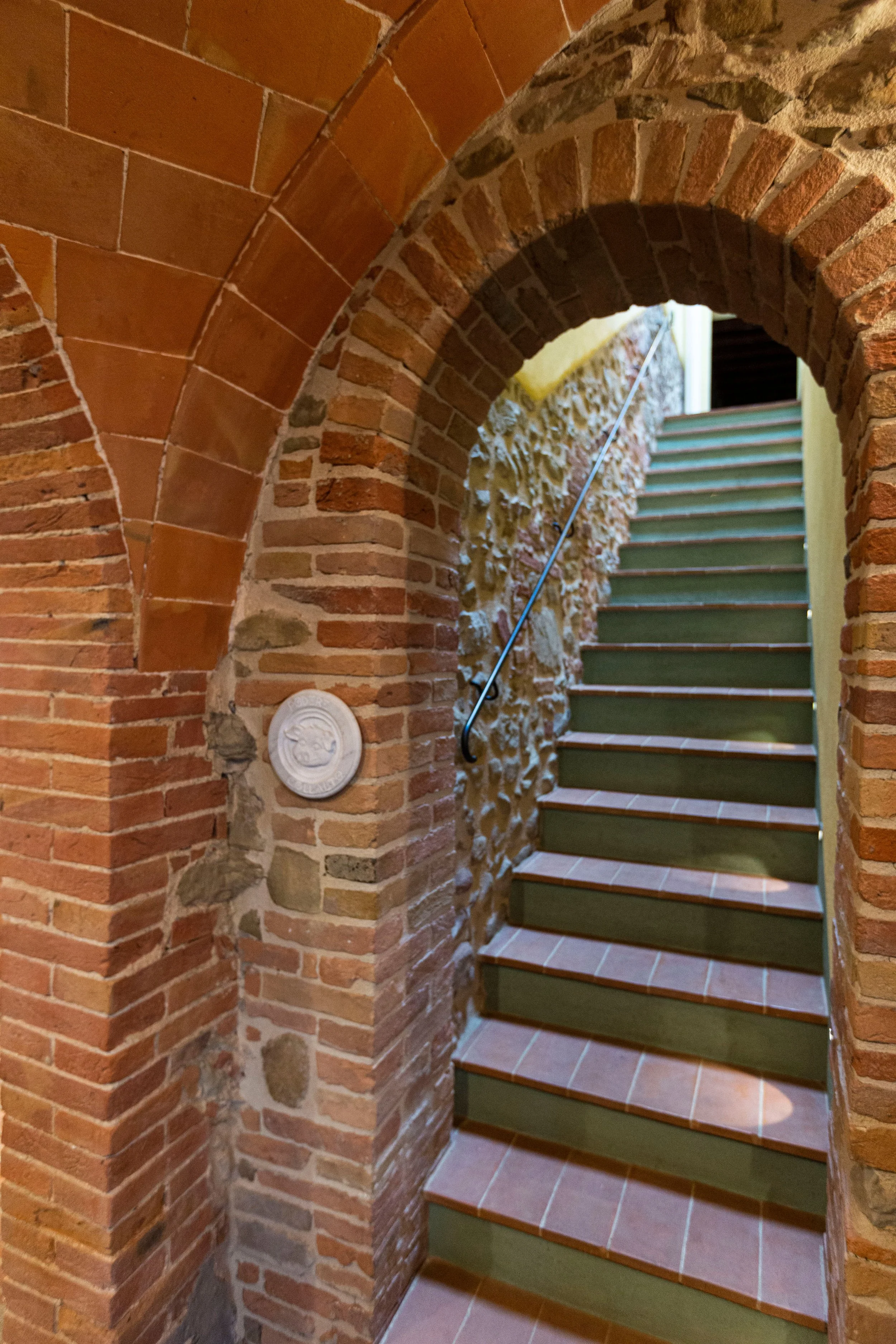 Interior view of a brick staircase with a curved brick archway and a handrail.