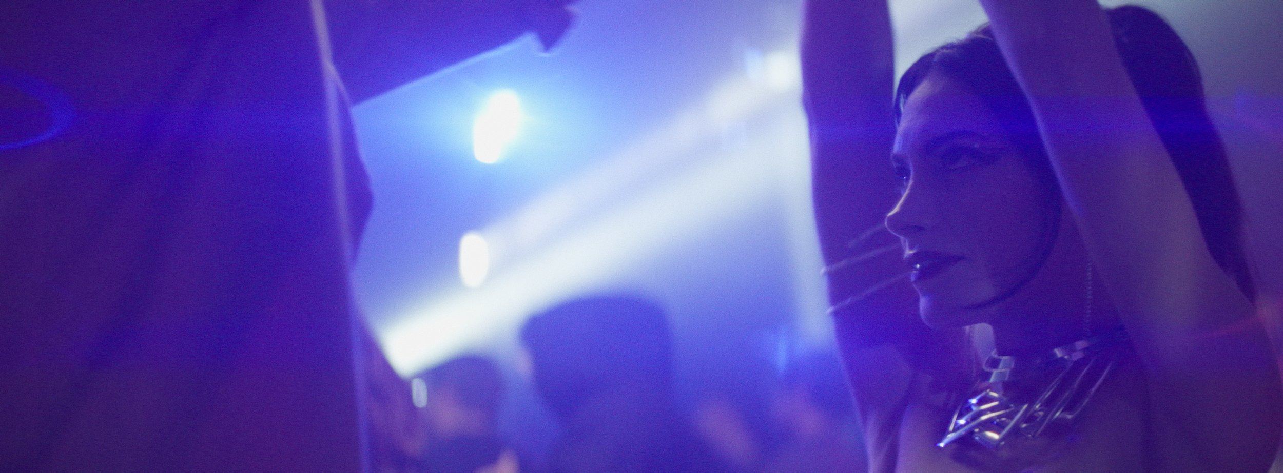 A woman with neon-colored makeup and jewelry in a dimly lit club, looking at a man who is out of focus.