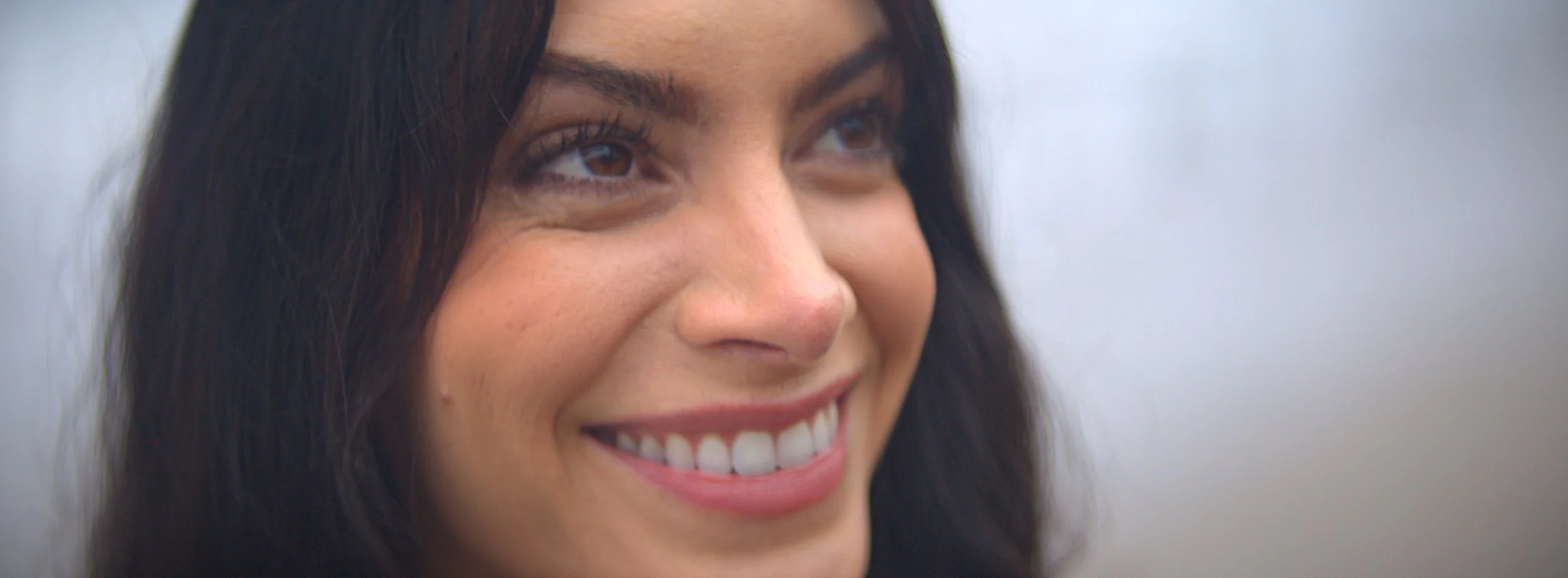 Close-up of a woman smiling, with long dark hair and light complexion.