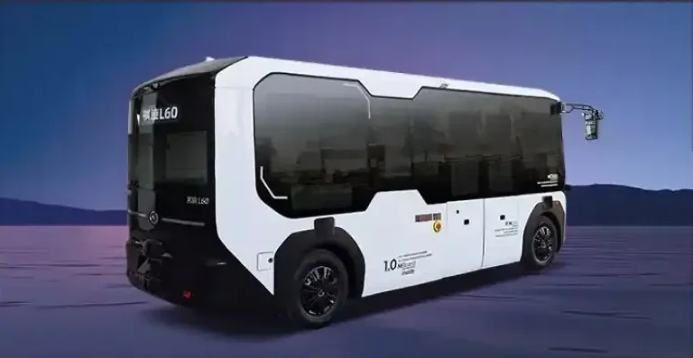 A futuristic autonomous electric bus with a sleek white and black design, large tinted windows, and a sensor on the front, set against a mountainous background.