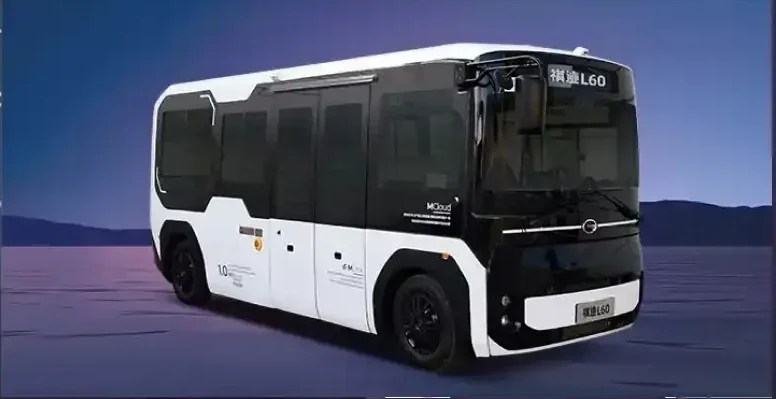 A black and white autonomous electric bus driving on a paved road with mountains in the background.