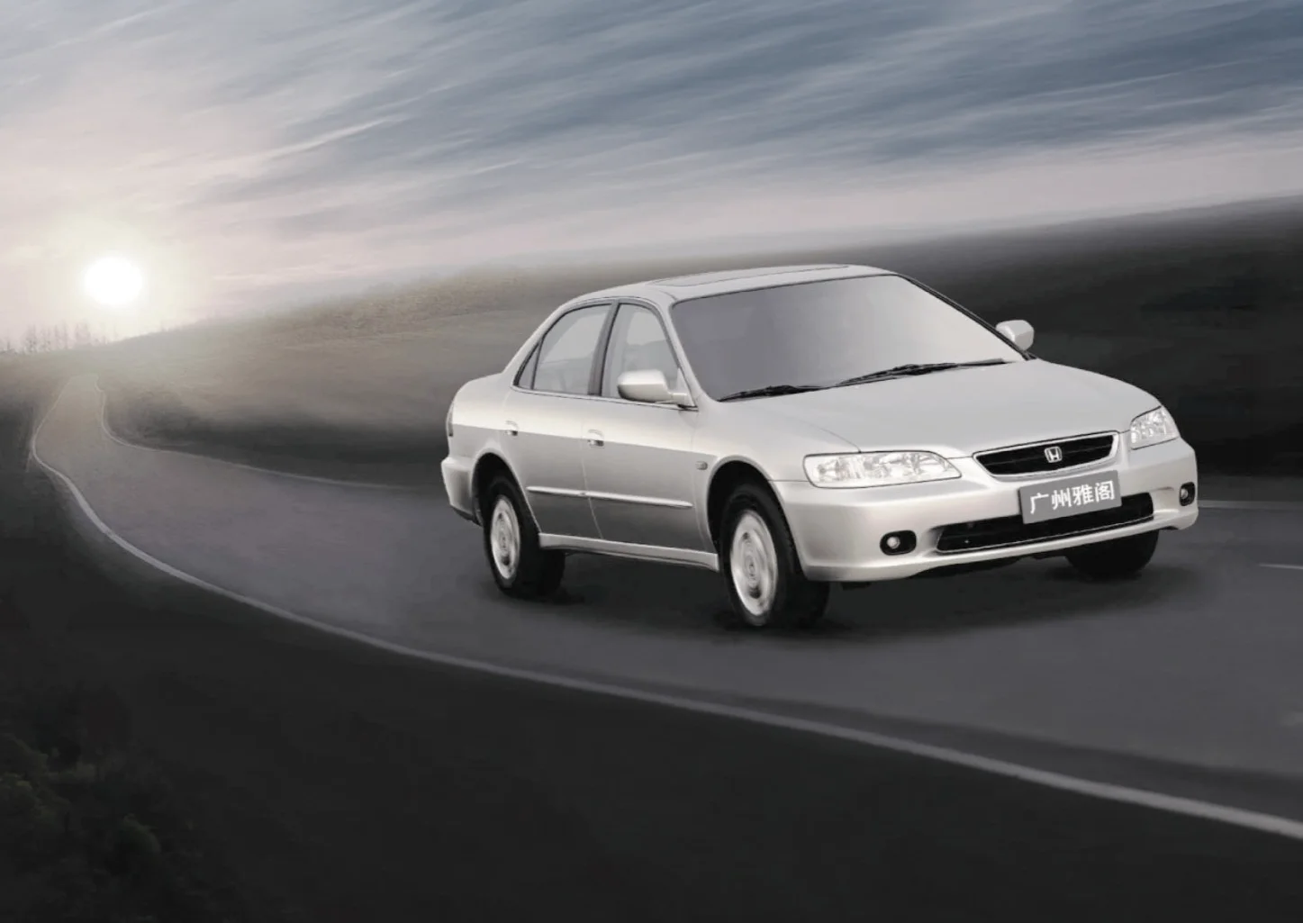 A silver sedan vehicle driving on a winding mountain road during sunset or sunrise.