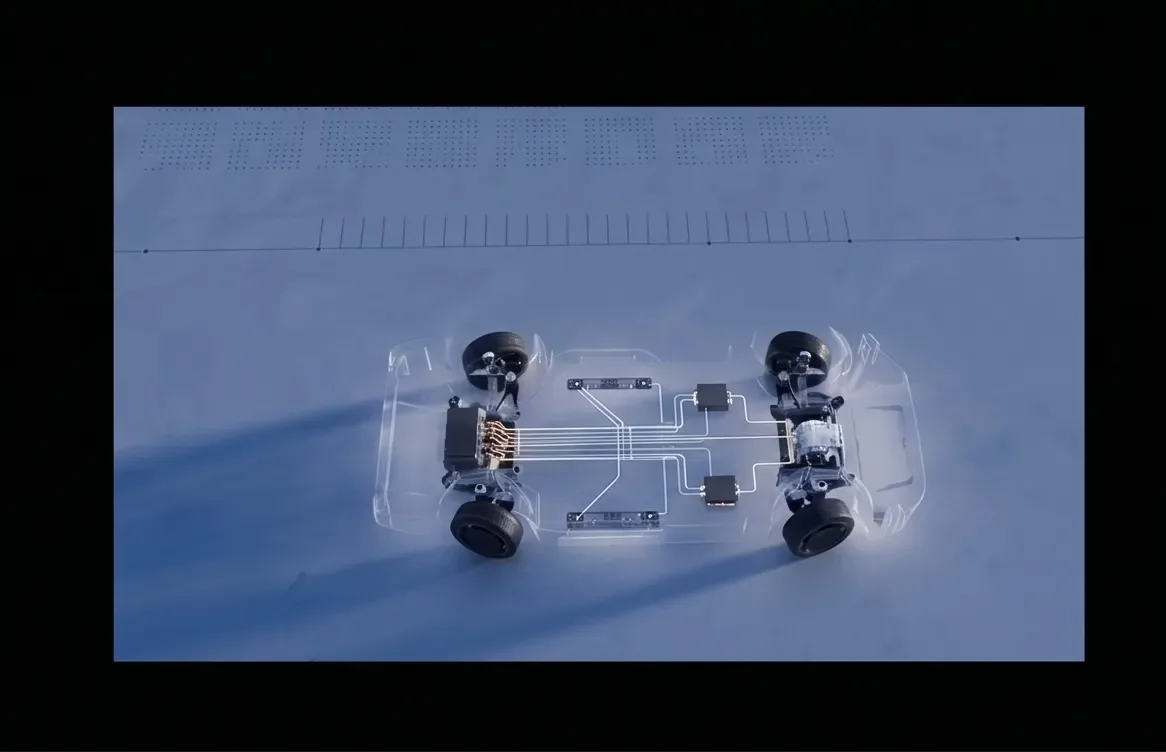 A transparent car chassis with electronic components and wiring inside, placed on a white surface with a ruler in the background.