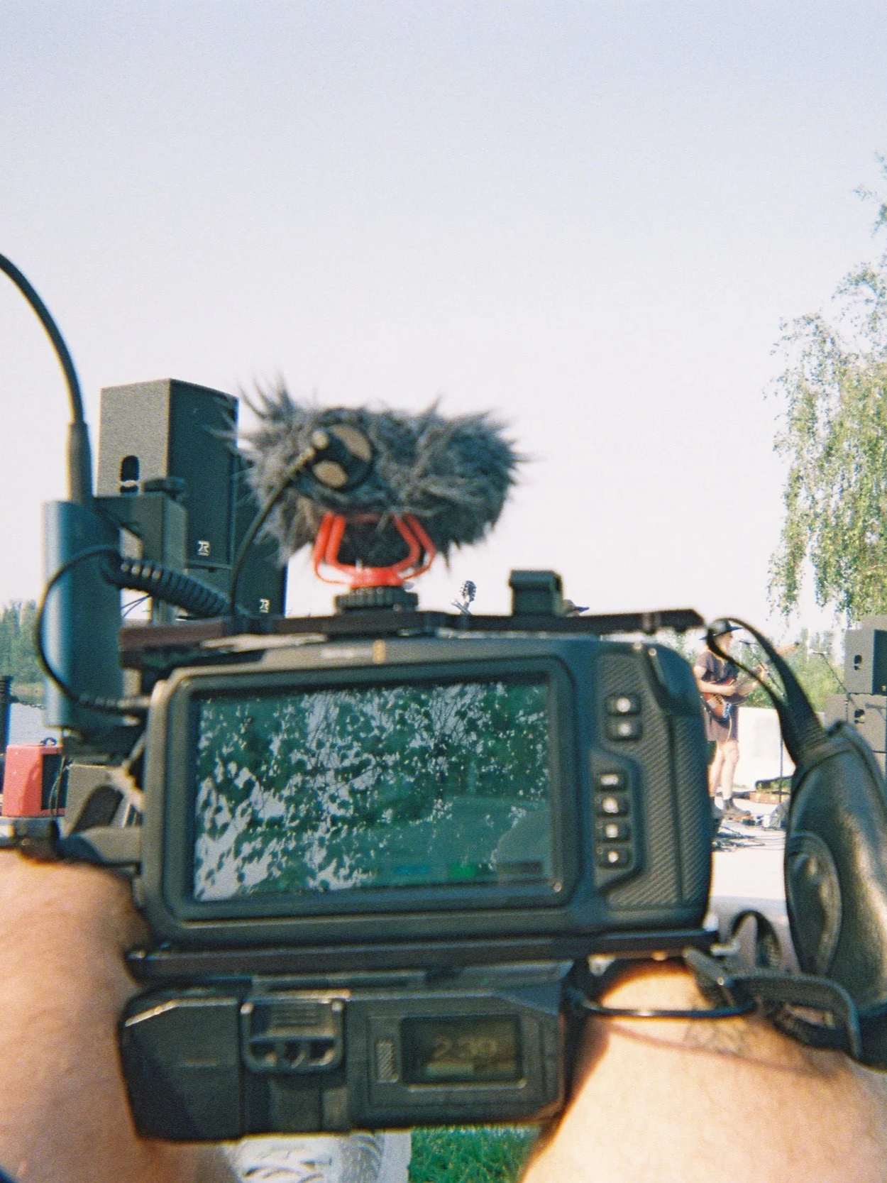A camera with a furry microphone mounted on top capturing a person in the background at an outdoor event.