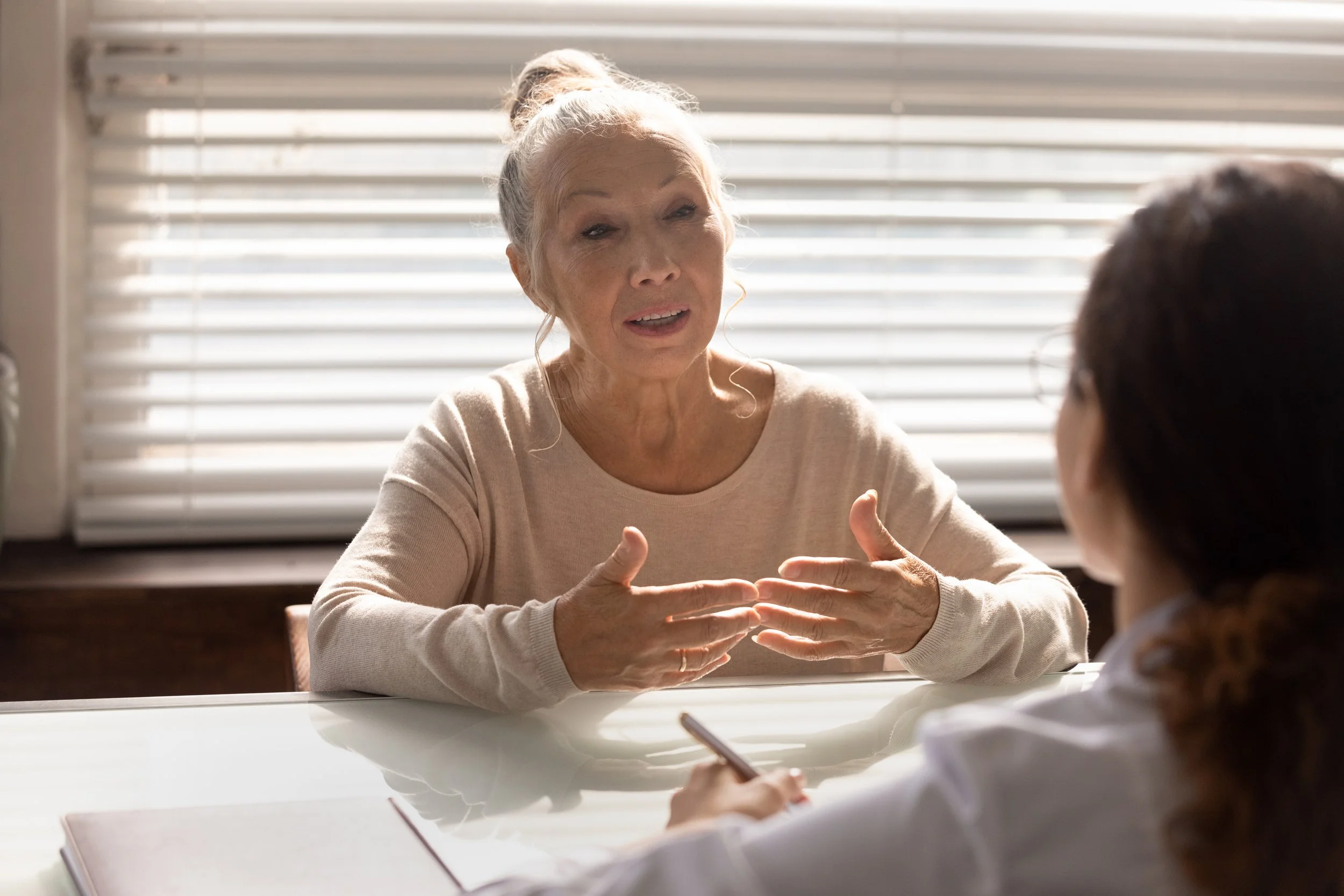 Older woman speaking confidently during a conversation at a home office table, illustrating preparation for a video interview in a career transition