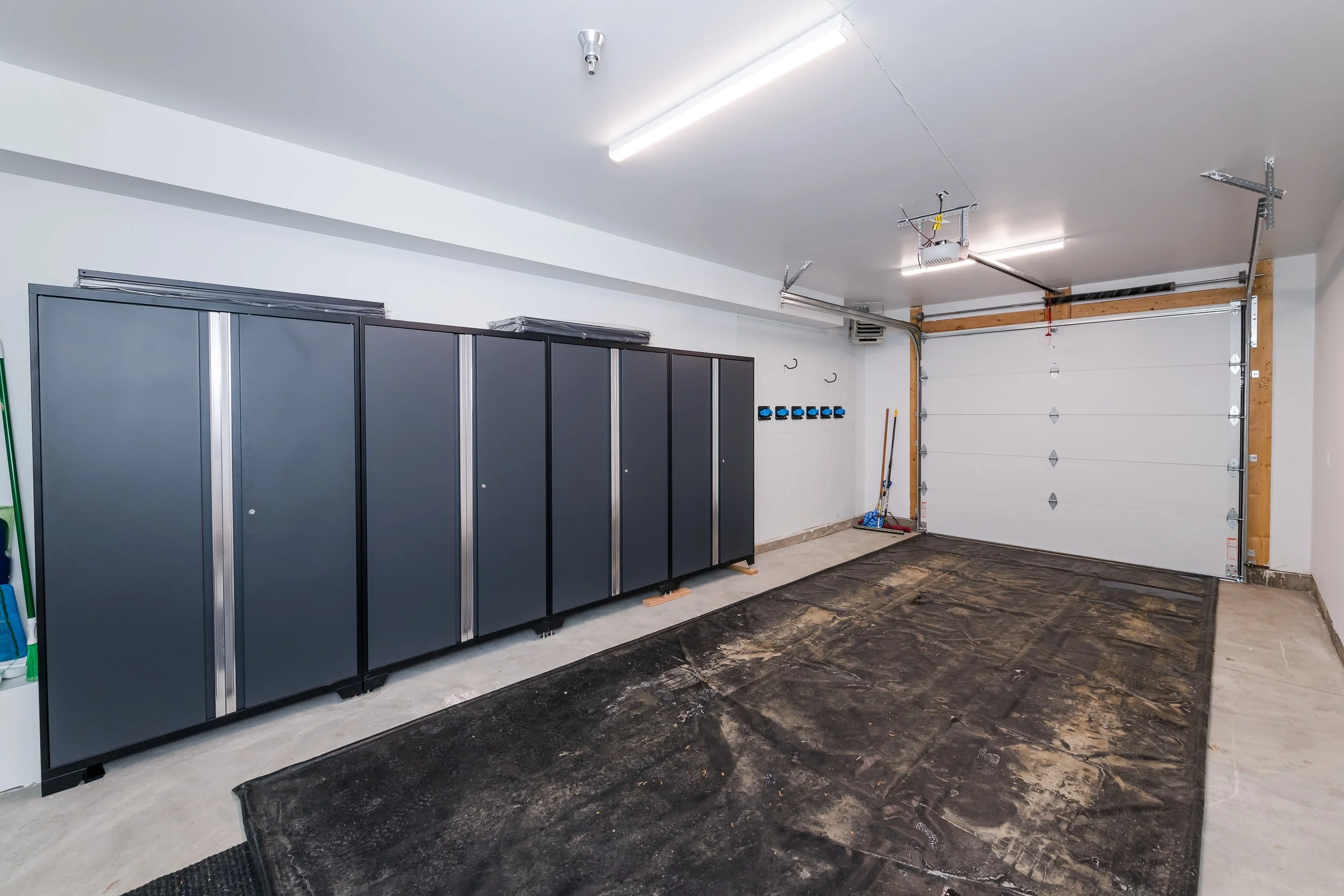 A garage interior with closed garage door, storage cabinets, and cleaning tools on the wall.