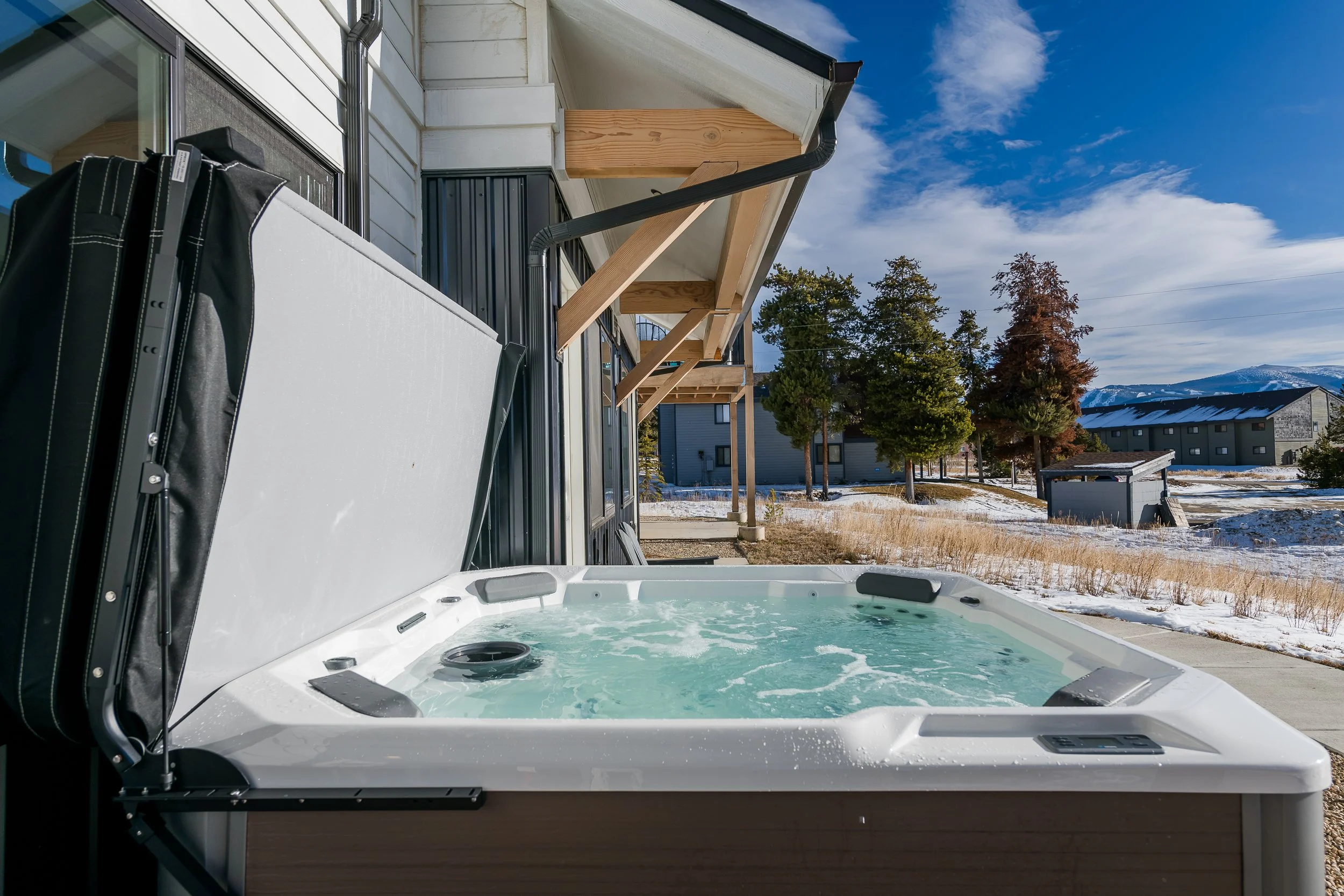 Hot tub installed on a balcony of a house with a view of snow-covered ground, trees, and distant mountains.