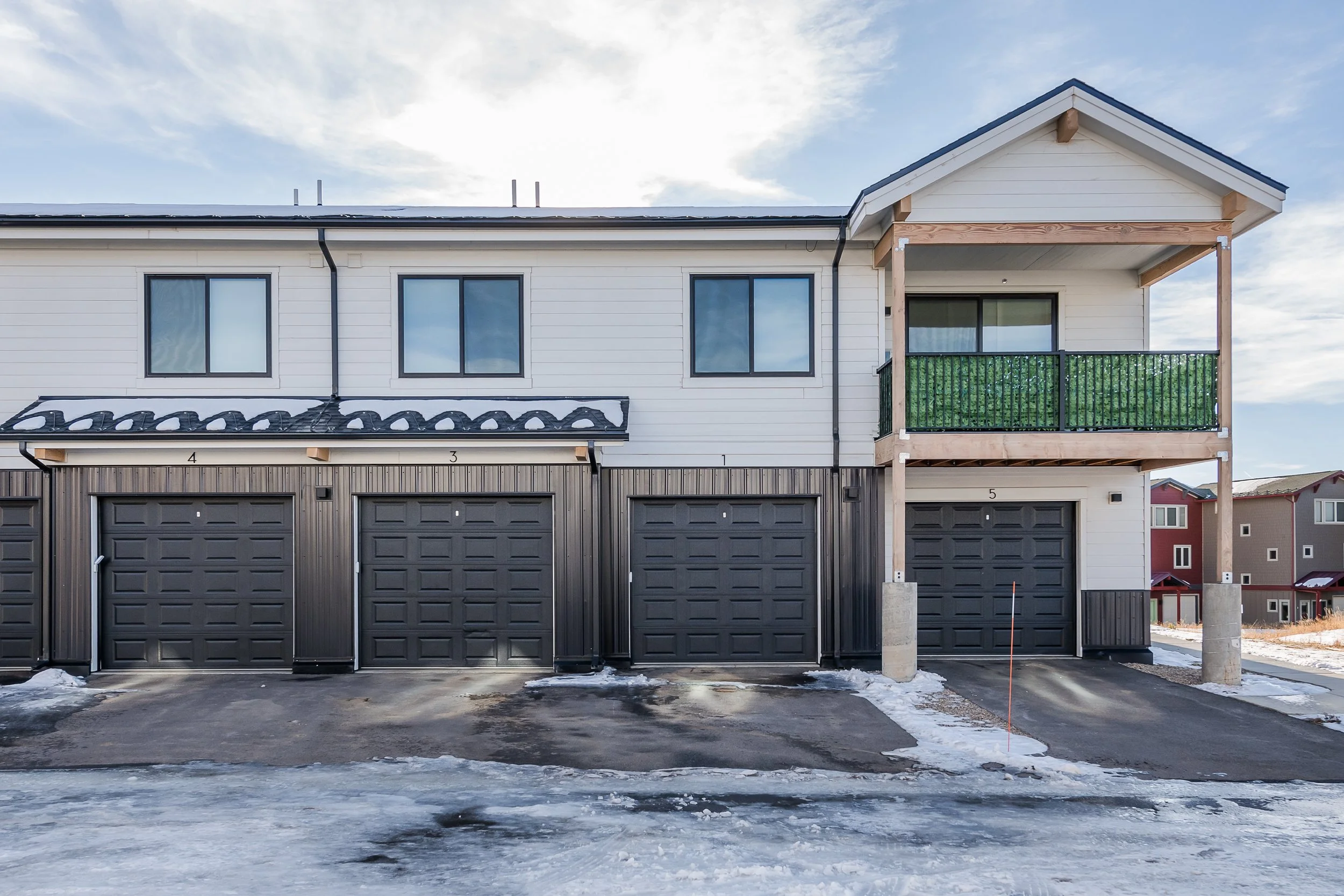 A row of modern townhouses with black garage doors, white siding, and small balconies, with some snow on the ground and under construction.