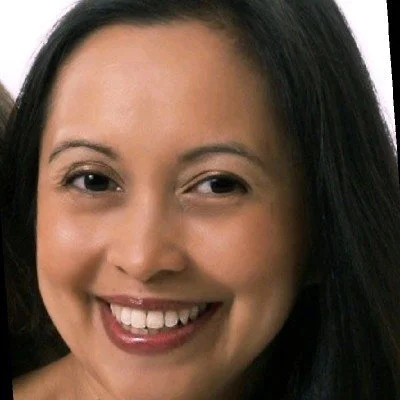 Close-up of a woman with long black hair, smiling with visible teeth.