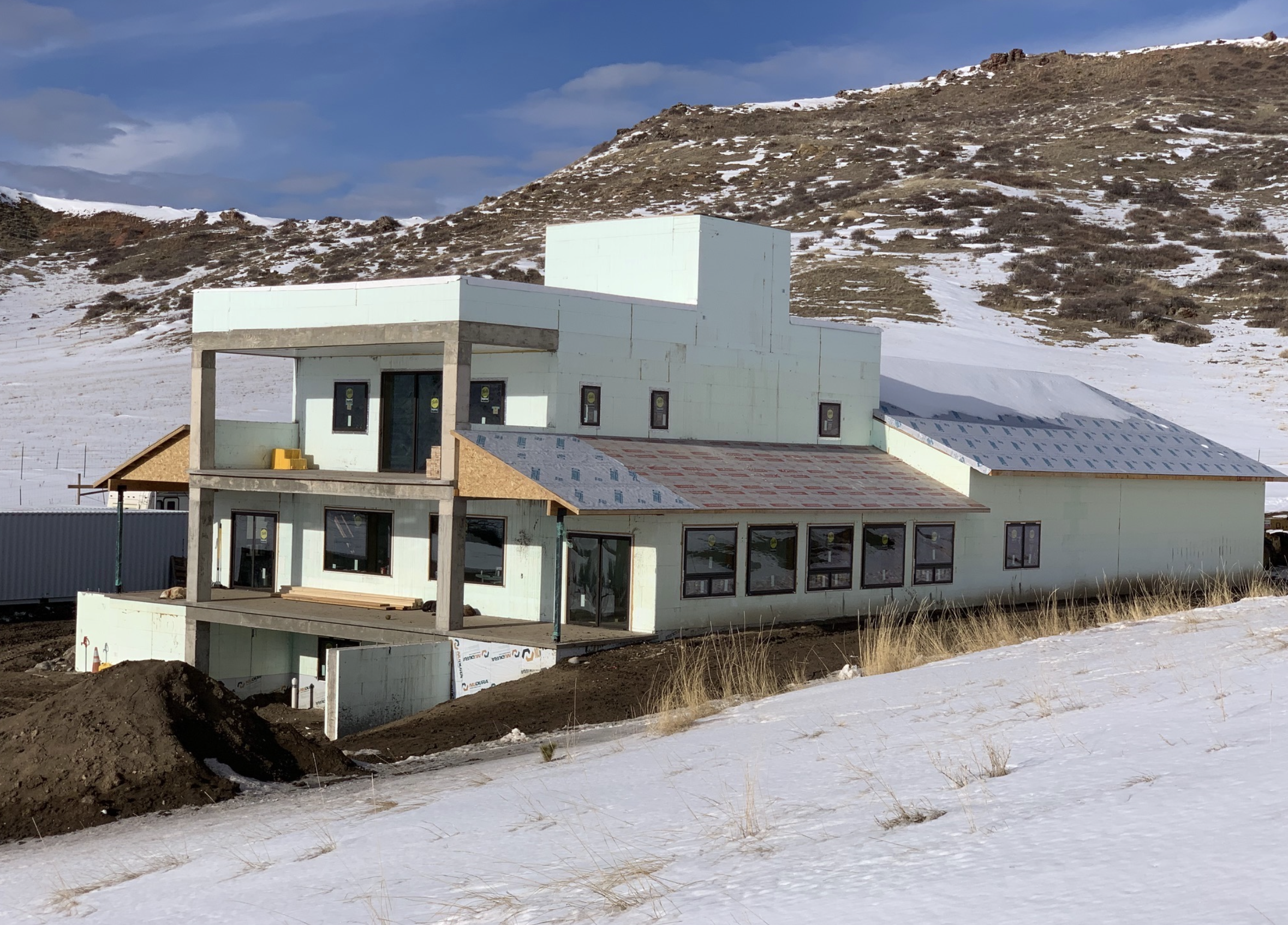 An insulated concrete form house under construction in a snowy landscape with mountains in the background.