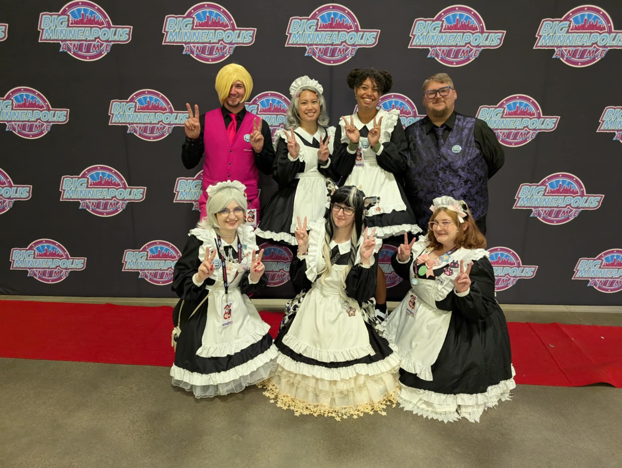 Group of people dressed in costumes posing on a red carpet in front of a backdrop that says 'Big Minneapolis Anime' multiple times.