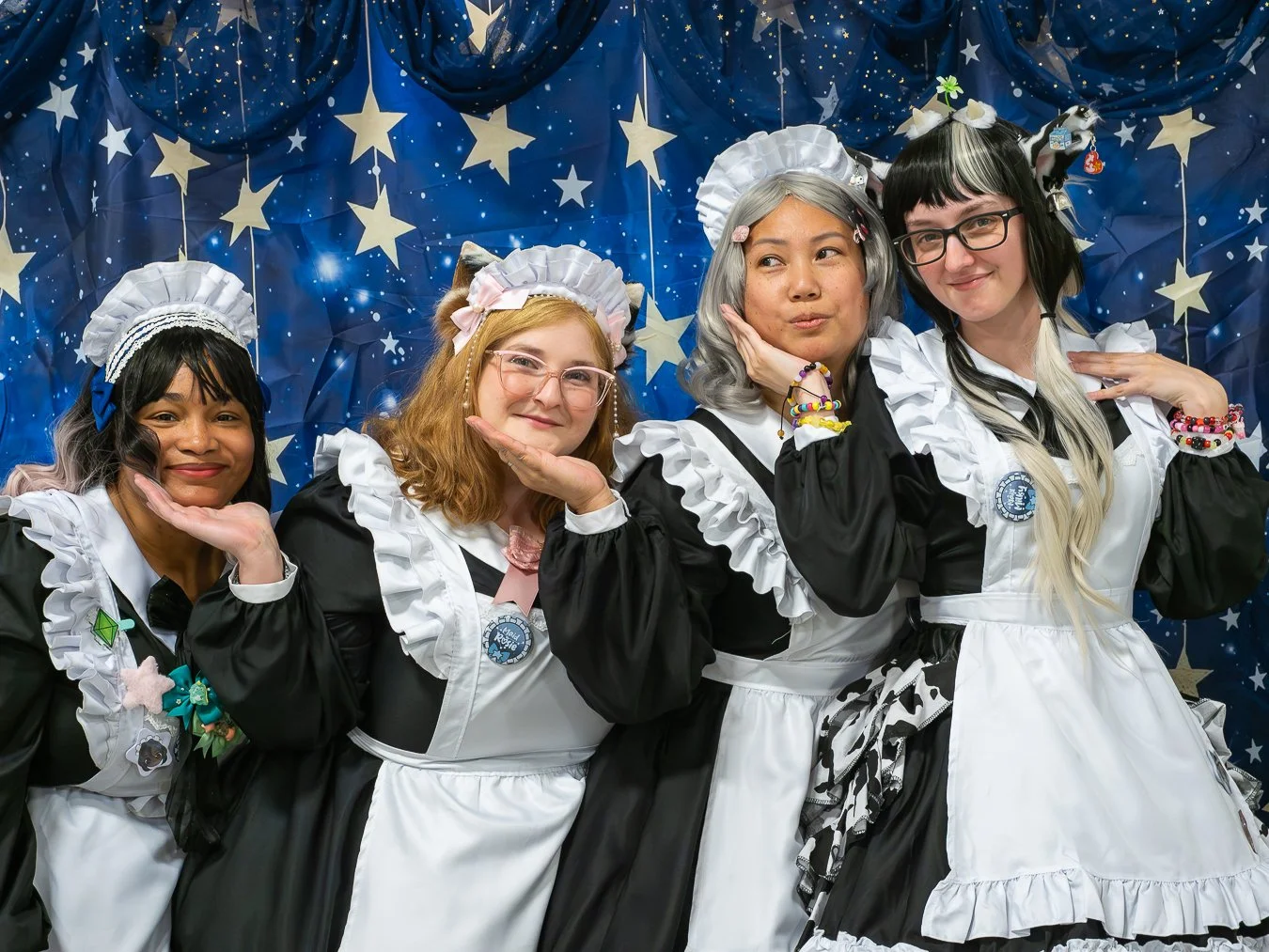 Four women dressed in maid costumes with animal ear headbands, posing in front of a starry blue backdrop with moon and star decorations.