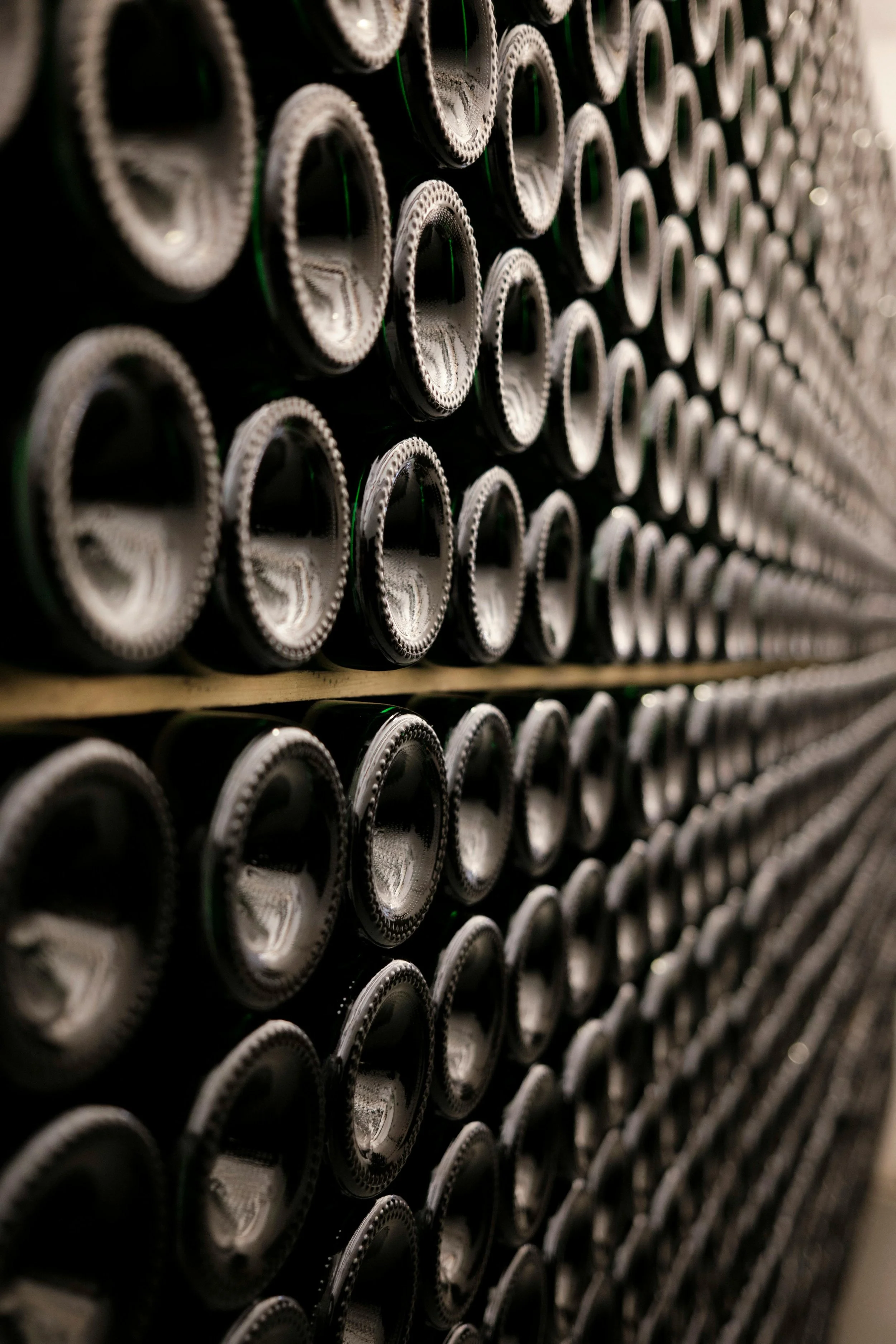 A wine cellar wall, bottles stacked end-out in dark wooden racks.