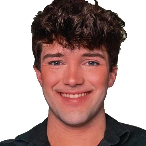 Close-up of a young man with curly brown hair, smiling and wearing a dark shirt.