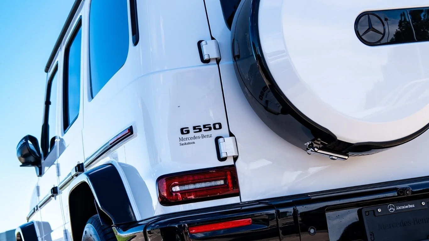 Close-up of the rear of a white Mercedes-Benz G550 SUV, showing the Mercedes-Benz logo, model badge, and spare tire on the back.