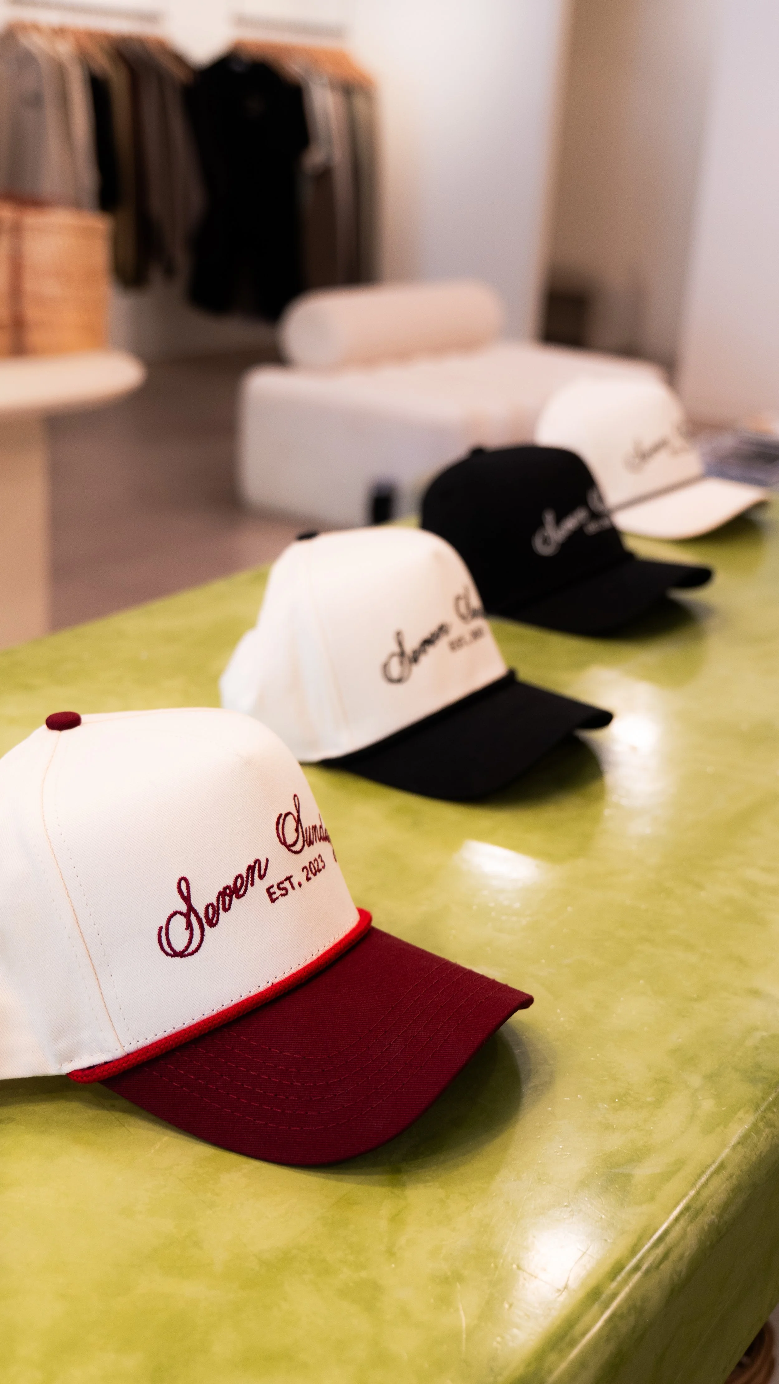 Four baseball caps with embroidered writing and colored brims on a green table.