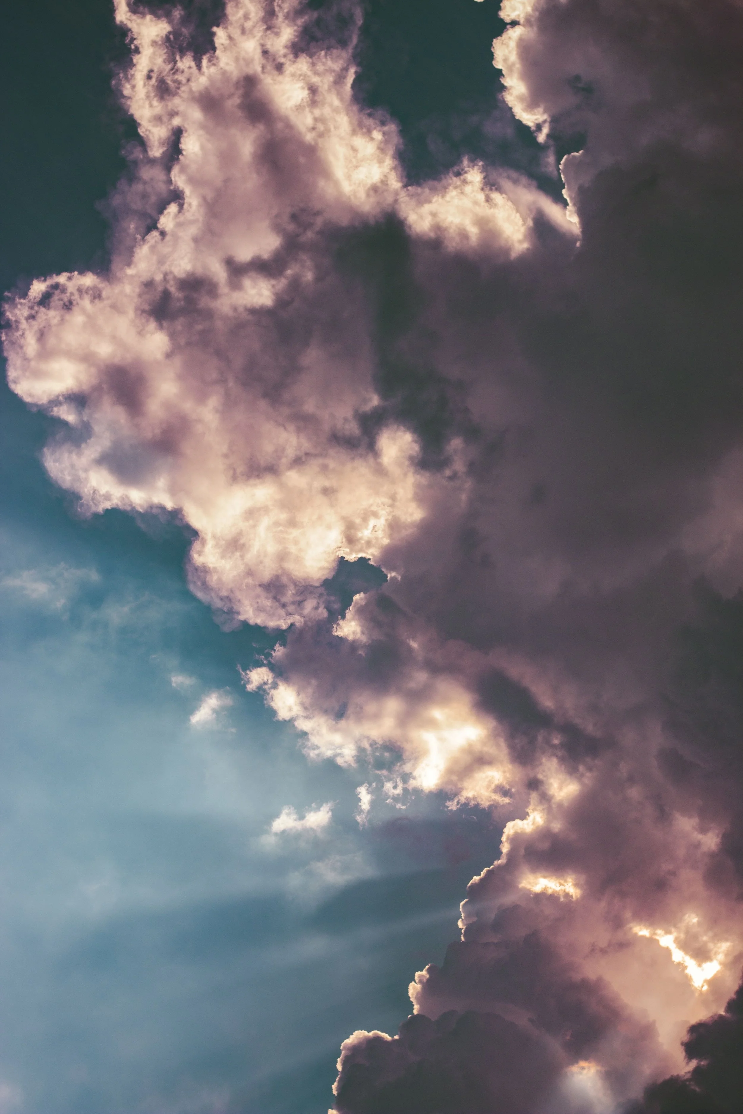 Clouds in the sky during sunset with sunlight shining through them, displaying shades of purple, pink, and gray.