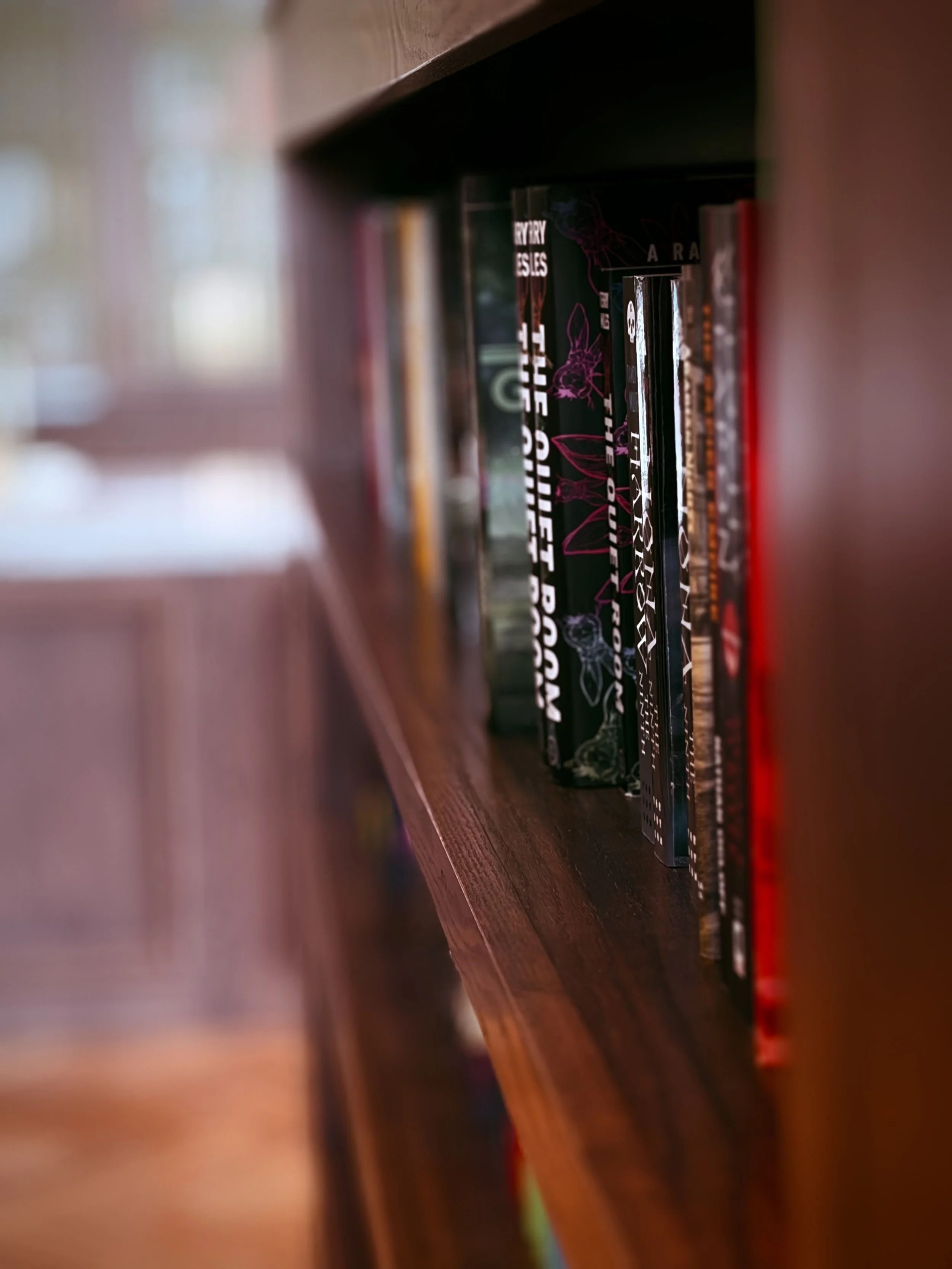 Books on a wooden shelf viewed through a narrow gap.