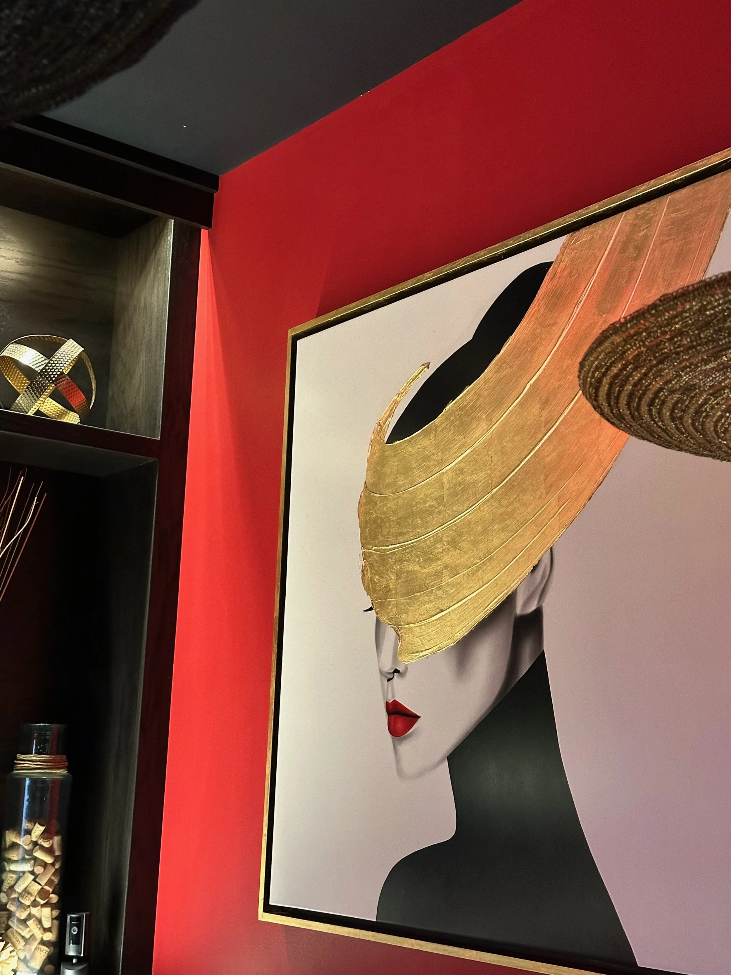 Close-up of a modern art piece featuring an oversized woman's face with bold red lips and a large gold leaf headdress, set against a red and white background.
