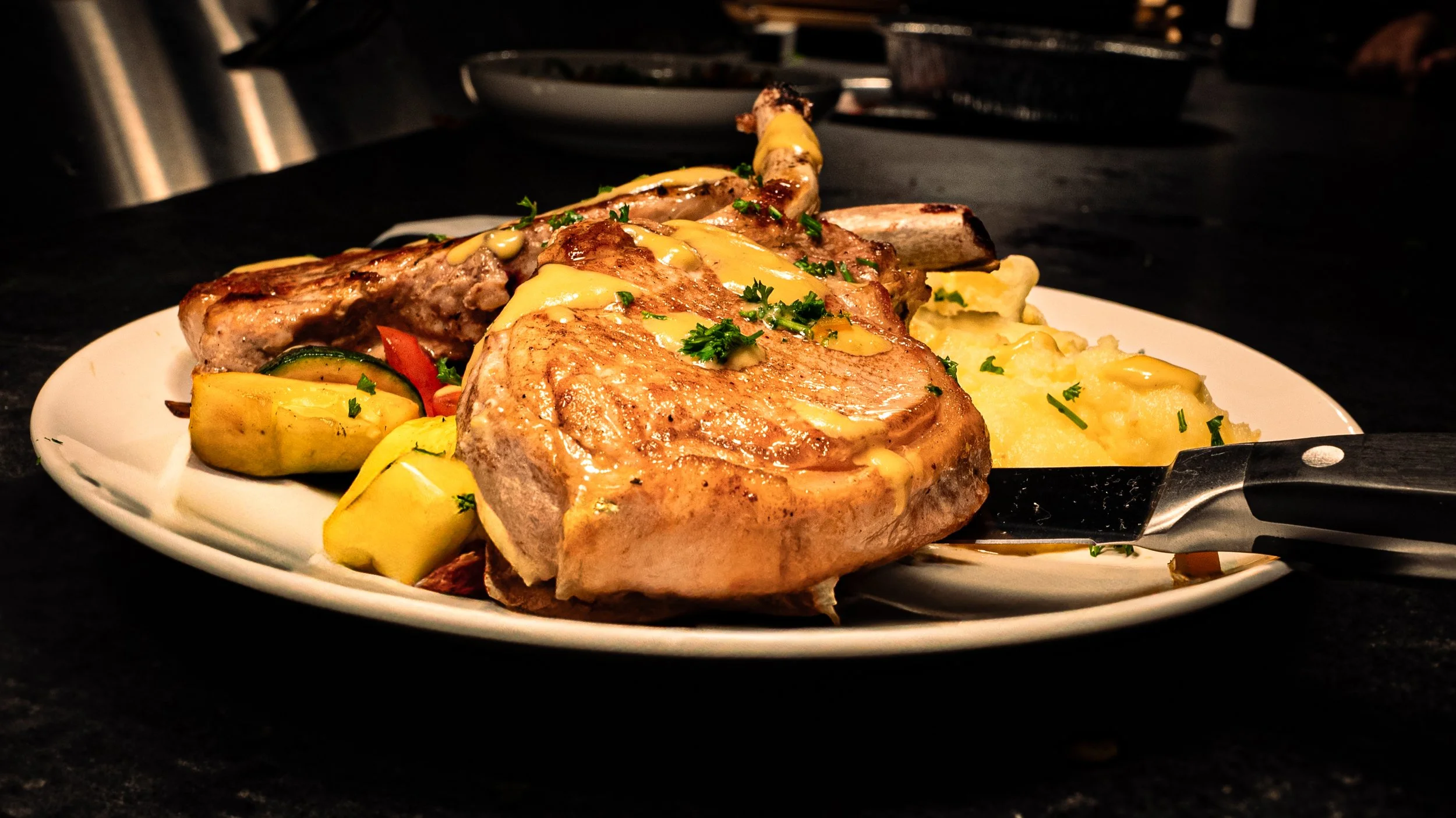 Cooked pork chop with gravy, mashed potatoes, and roasted vegetables on a white plate.