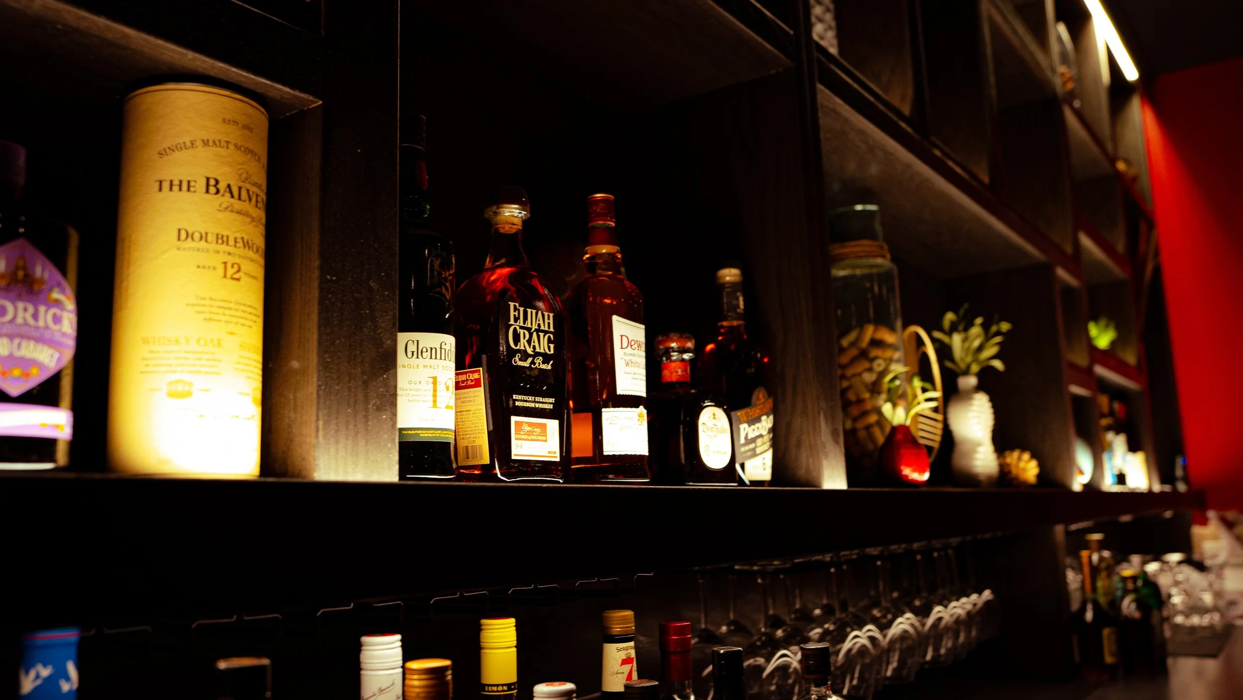 Shelf with various bottles of liquor, including whiskey, bourbon, and other spirits, in a dimly lit bar or liquor store.