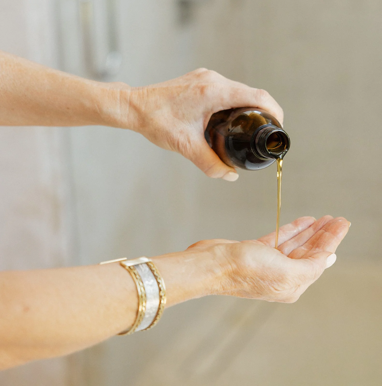 Pouring herbal oil from an amber glass bottle into an open hand.