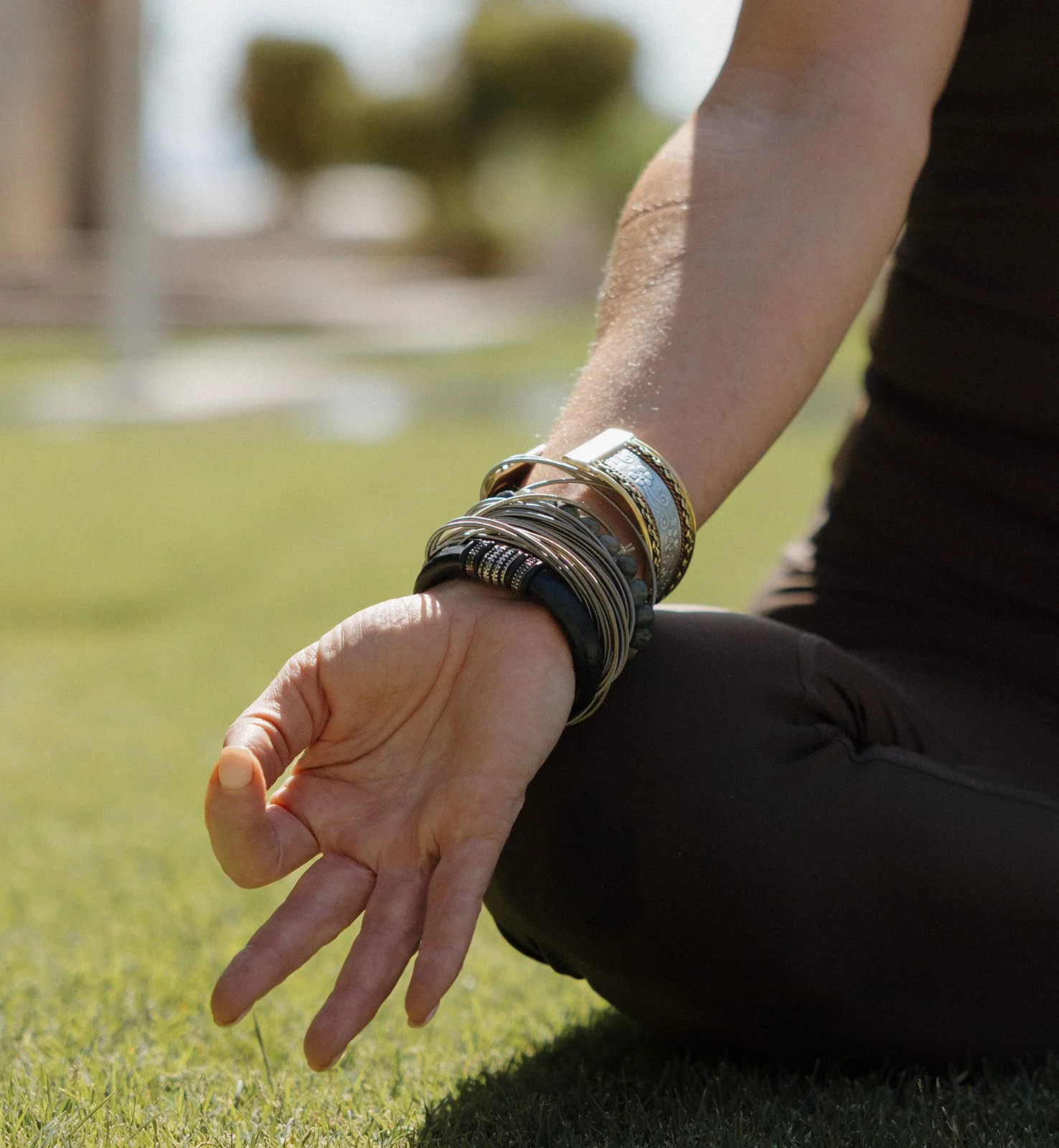 Person practicing meditation outdoors, sitting with legs crossed and hand resting on the knee, on a grassy surface.