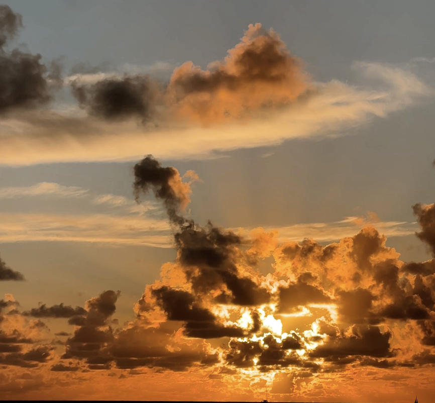 Sunset behind clouds with orange and gold hues.