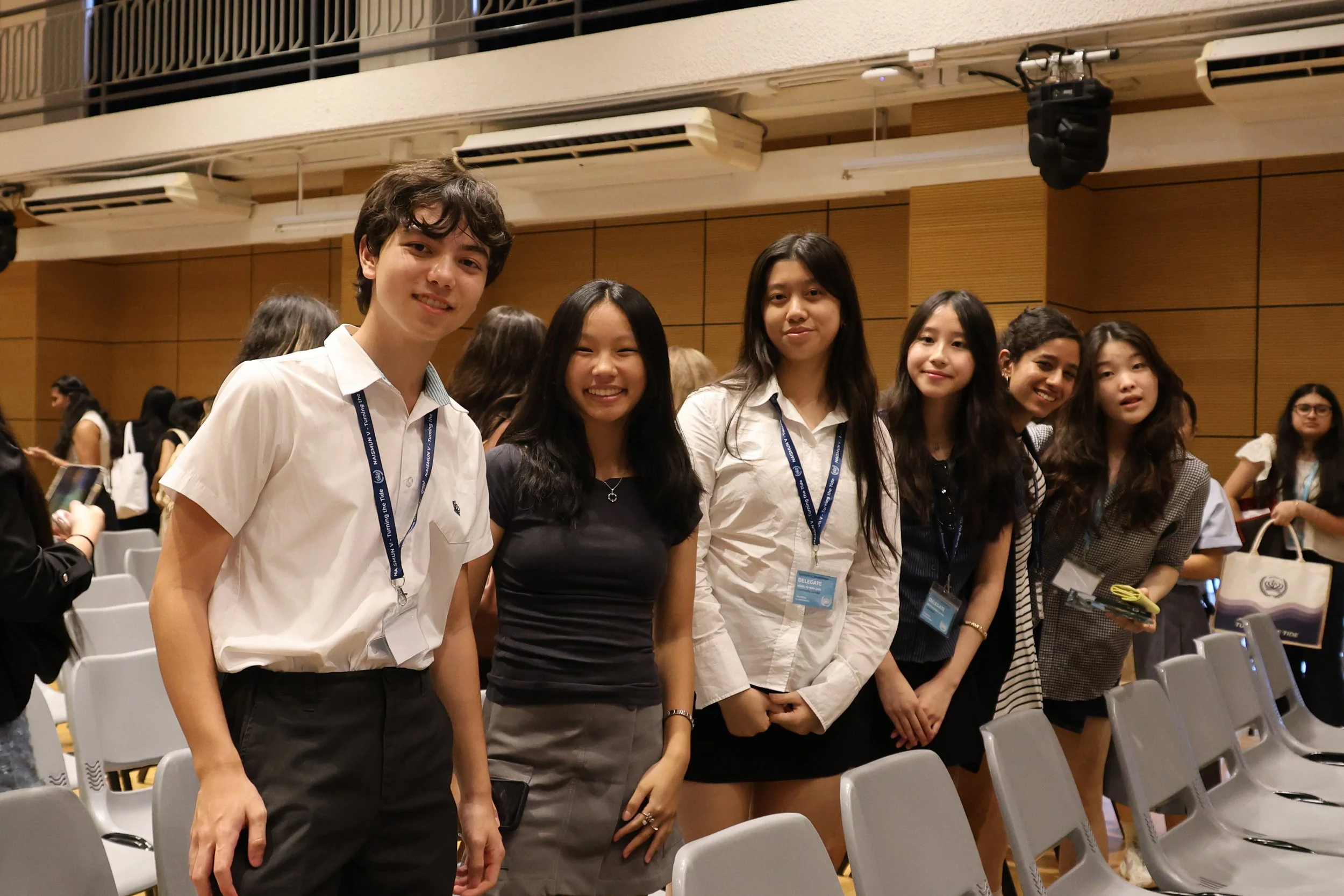 Group of young women and men standing together in a conference room, smiling for the camera. They are wearing conference badges and casual business attire.