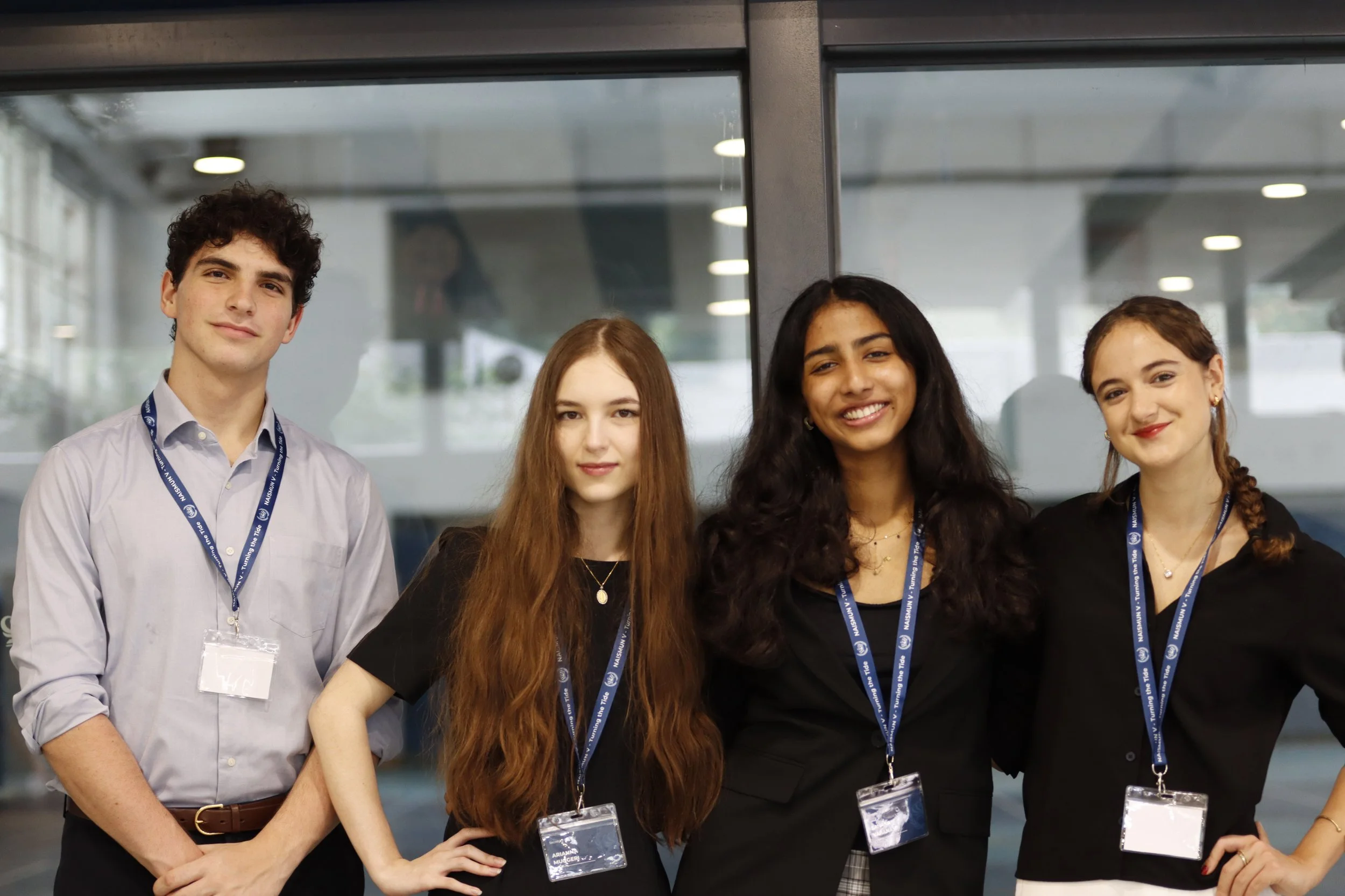 Four young adults standing side by side indoors, wearing conference badges and lanyards.