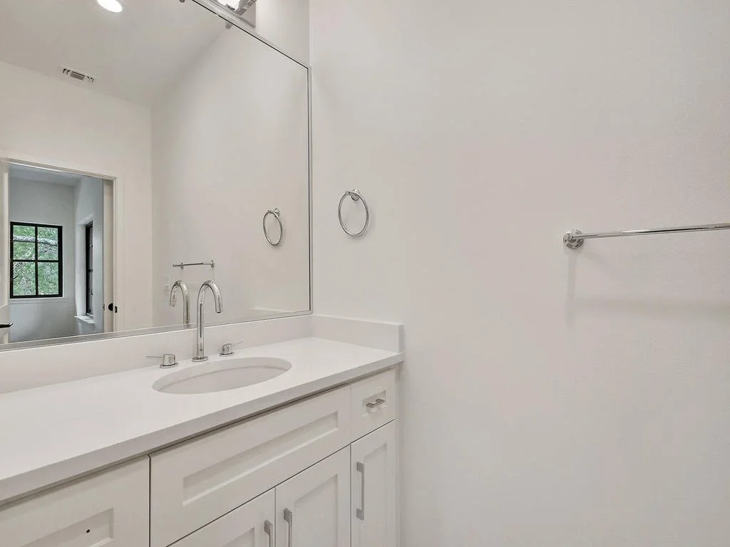 A minimalist bathroom with a white vanity, large mirror, and towel rings on the wall.