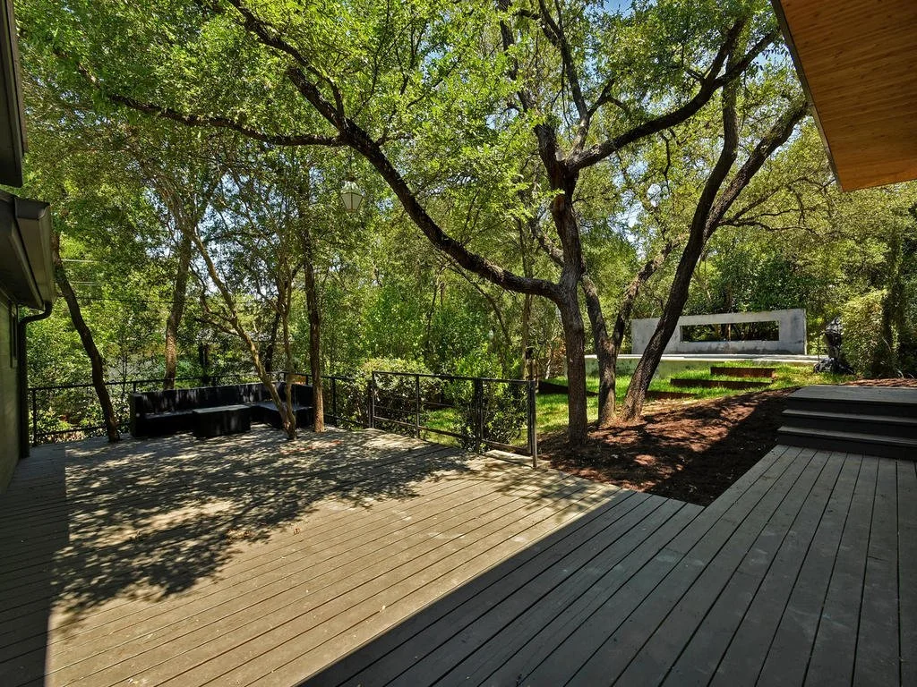 Wooden deck with outdoor seating surrounded by trees and greenery in a backyard.