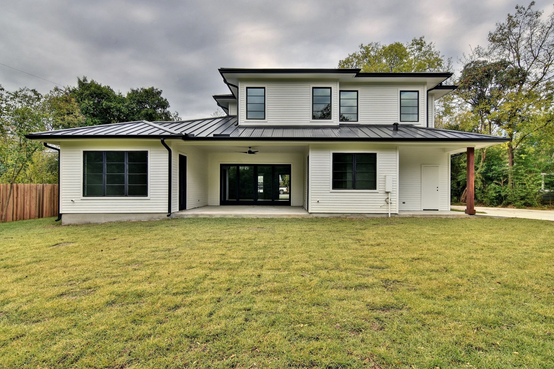 A modern two-story house with white siding, black-framed windows, and a metal roof, with a grassy yard and trees in the background.