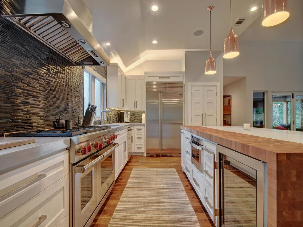 Modern kitchen with white cabinets, stainless steel appliances, a wooden island, pendant lights, and a textured backsplash.