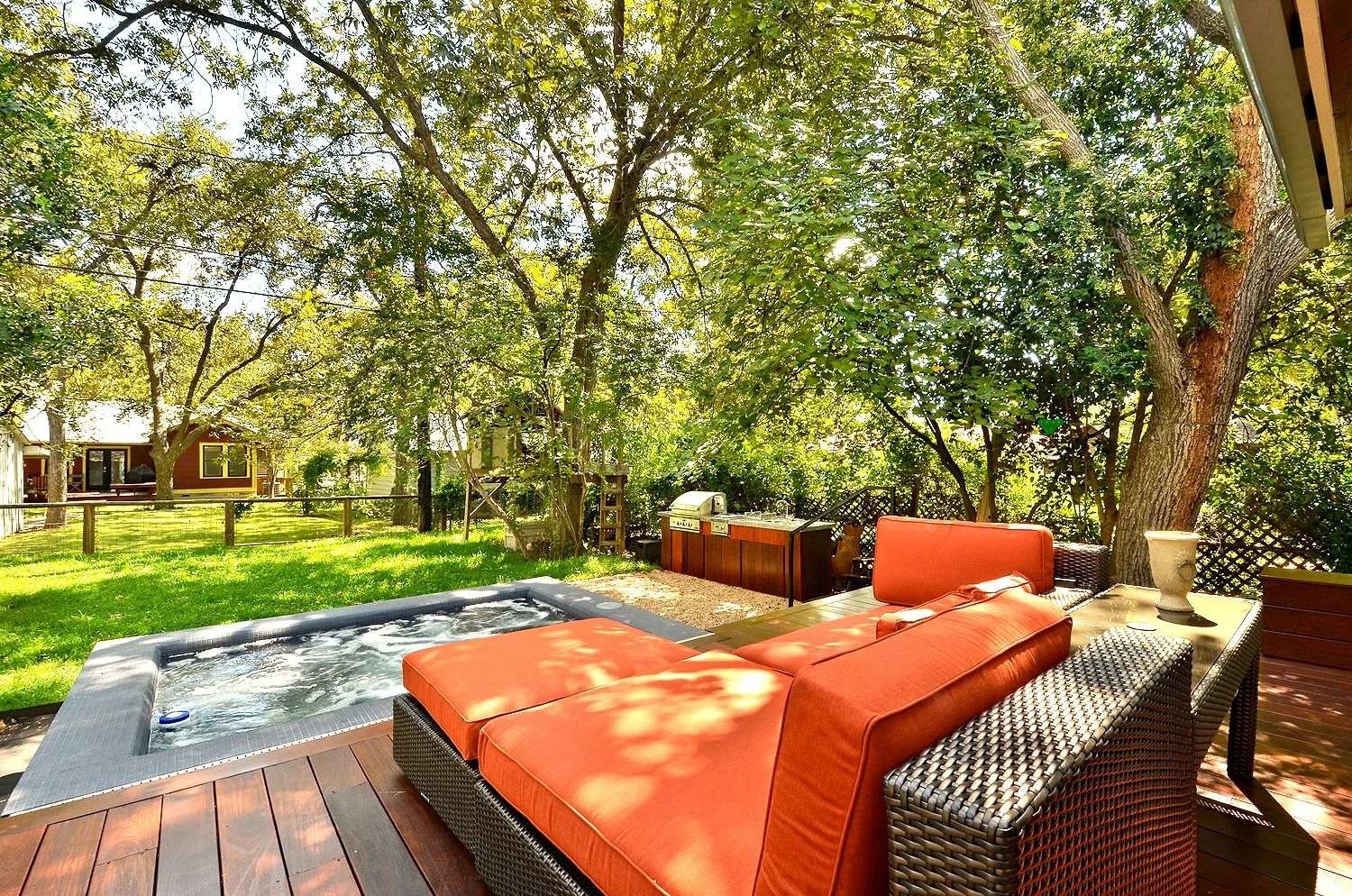 Backyard with orange patio furniture, hot tub, trees, and a barbecue grill on a sunny day