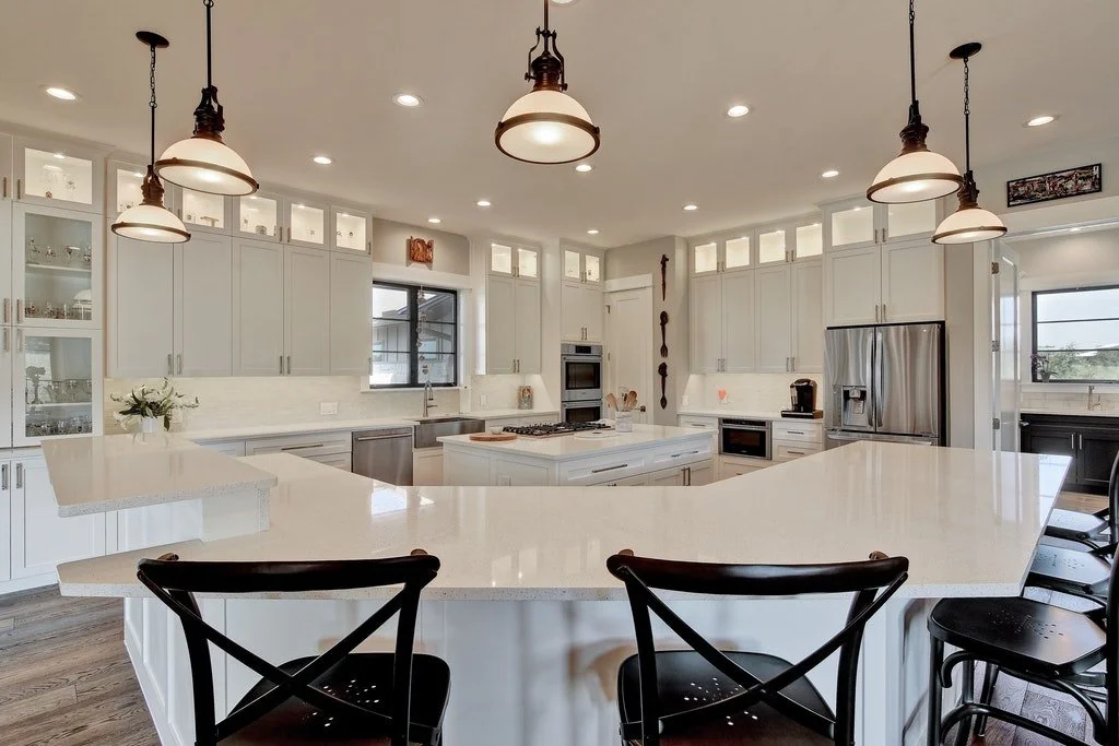 Modern kitchen with white cabinets, a kitchen island, stainless steel appliances, pendant lights, and bar stools.