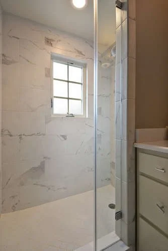 Modern bathroom with a marble shower, small window, and part of a white vanity.