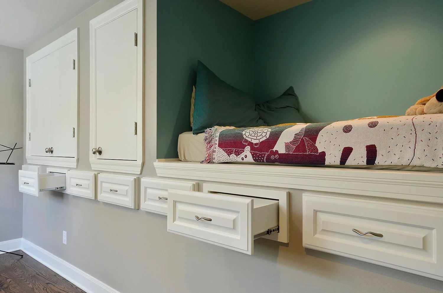 Built-in wall storage with cabinets and drawers above a window seat with pillows and a blanket.