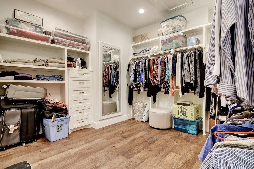 Walk-in closet filled with clothes, storage bins, suitcases, and a full-length mirror.