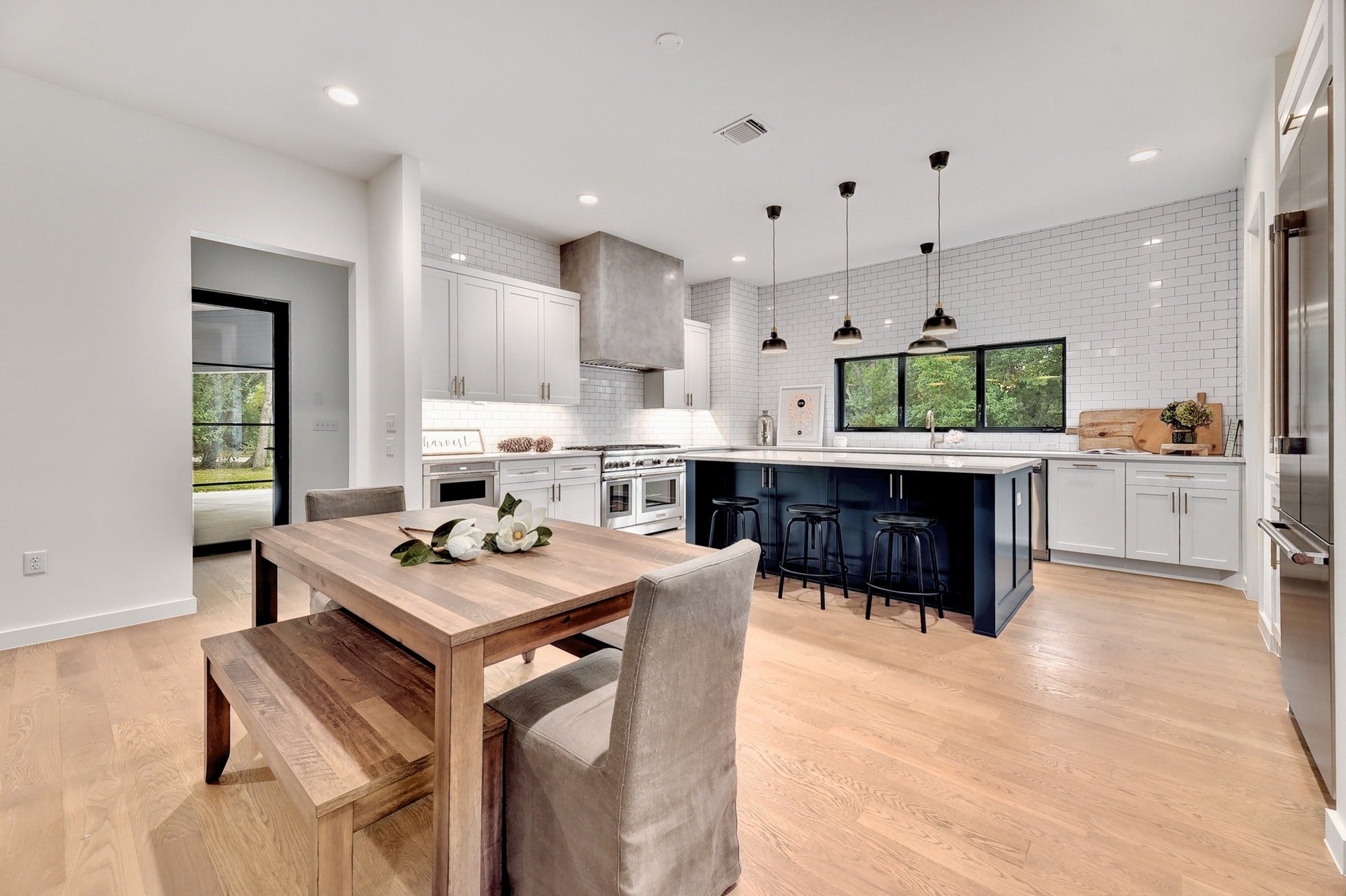 Open-concept kitchen with white cabinets, a large island with black stools, pendant lighting, and a window overlooking greenery.