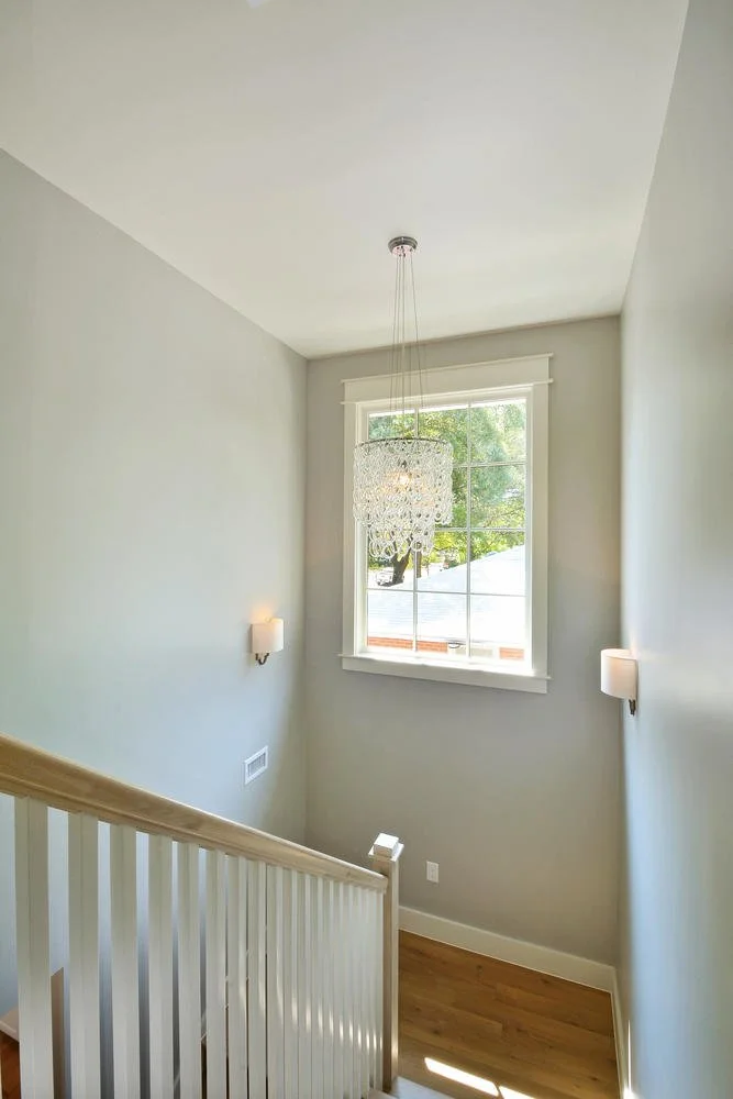 View of a stairwell with a large window, a chandelier, and wall-mounted lights, with hardwood flooring.