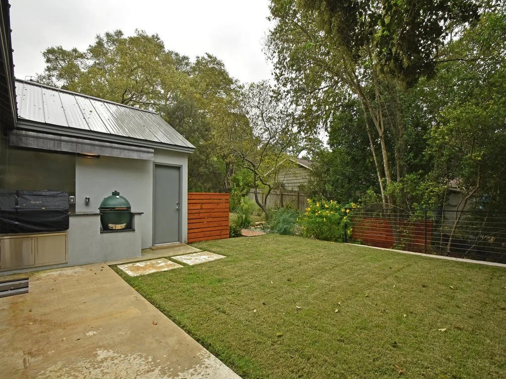 Backyard with a grassy lawn, trees, a concrete patio, a gray shed, and a black grill.