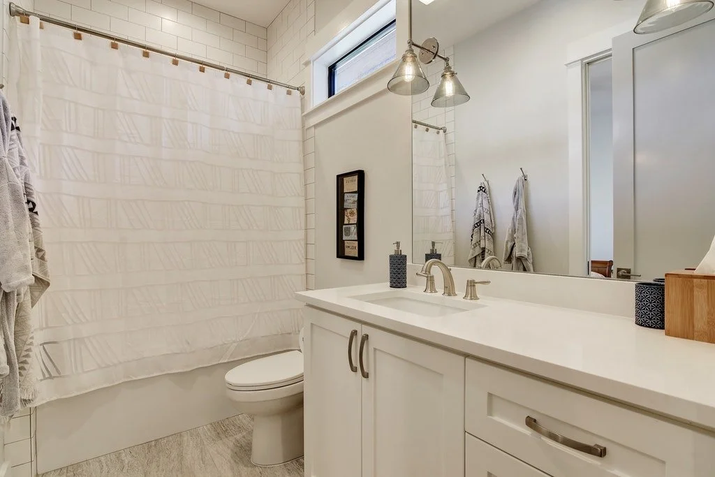 Bathroom with white vanity, large mirror, shower with curtain, towel racks, and neutral decor.