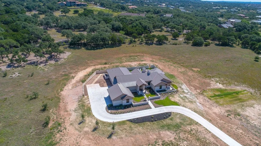 Aerial view of a single-family house with a curved driveway, surrounded by open land and trees.