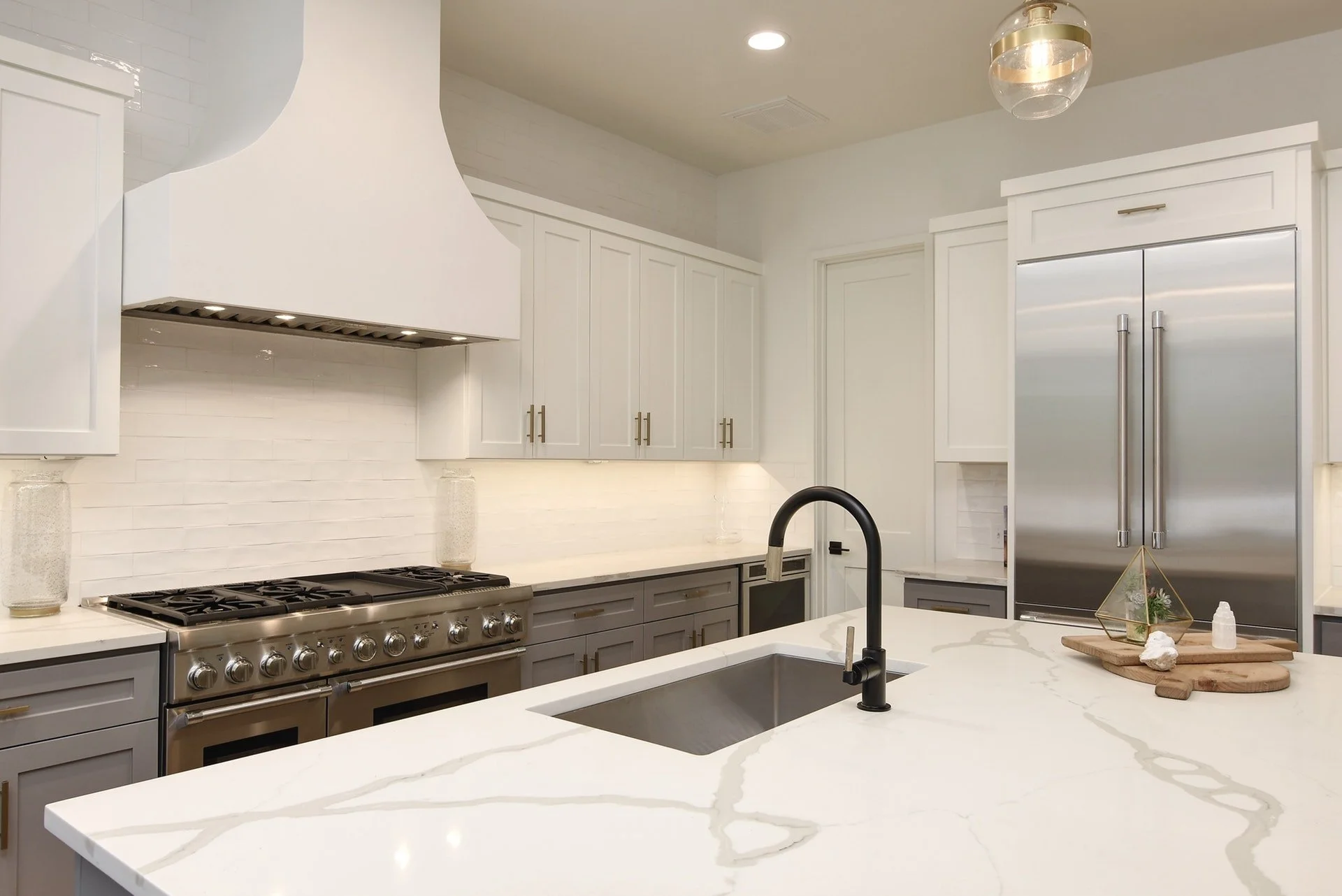 Modern white and gray kitchen with marble island, stainless steel appliances, white cabinets, and black faucet.