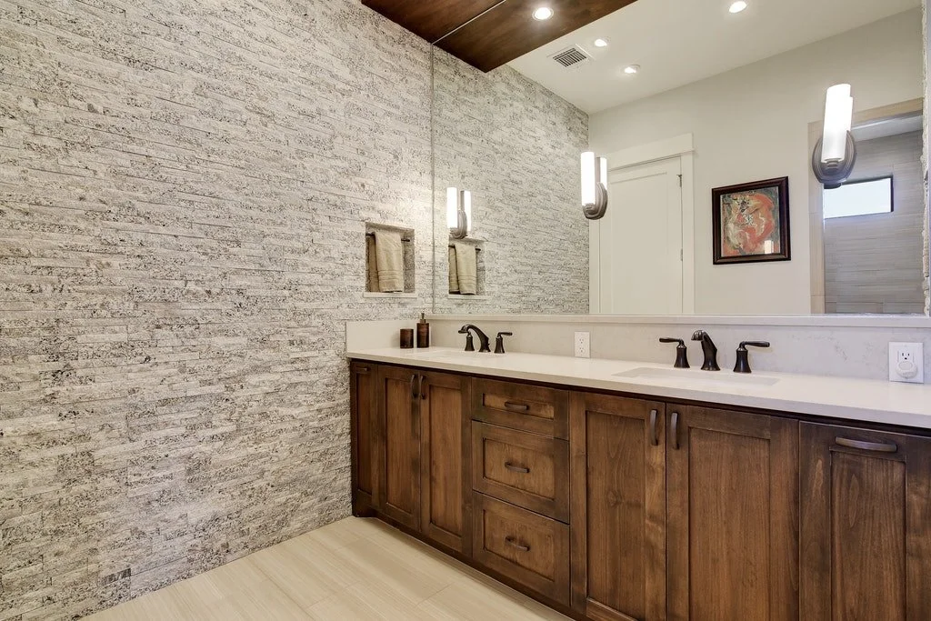 Bathroom with a double sink vanity, large mirror, textured light-colored brick wall, and modern wall sconces.