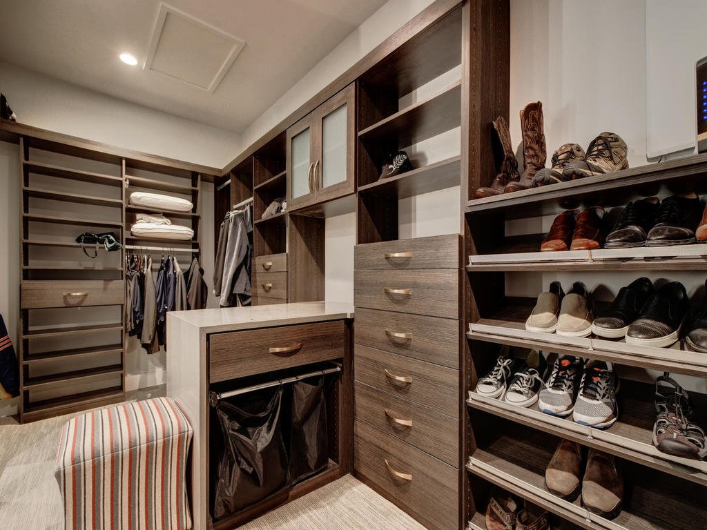 A walk-in closet with wooden shelving units, a clothing hanging rod, drawers, and shelves for shoes, with clothes and shoes organized inside.